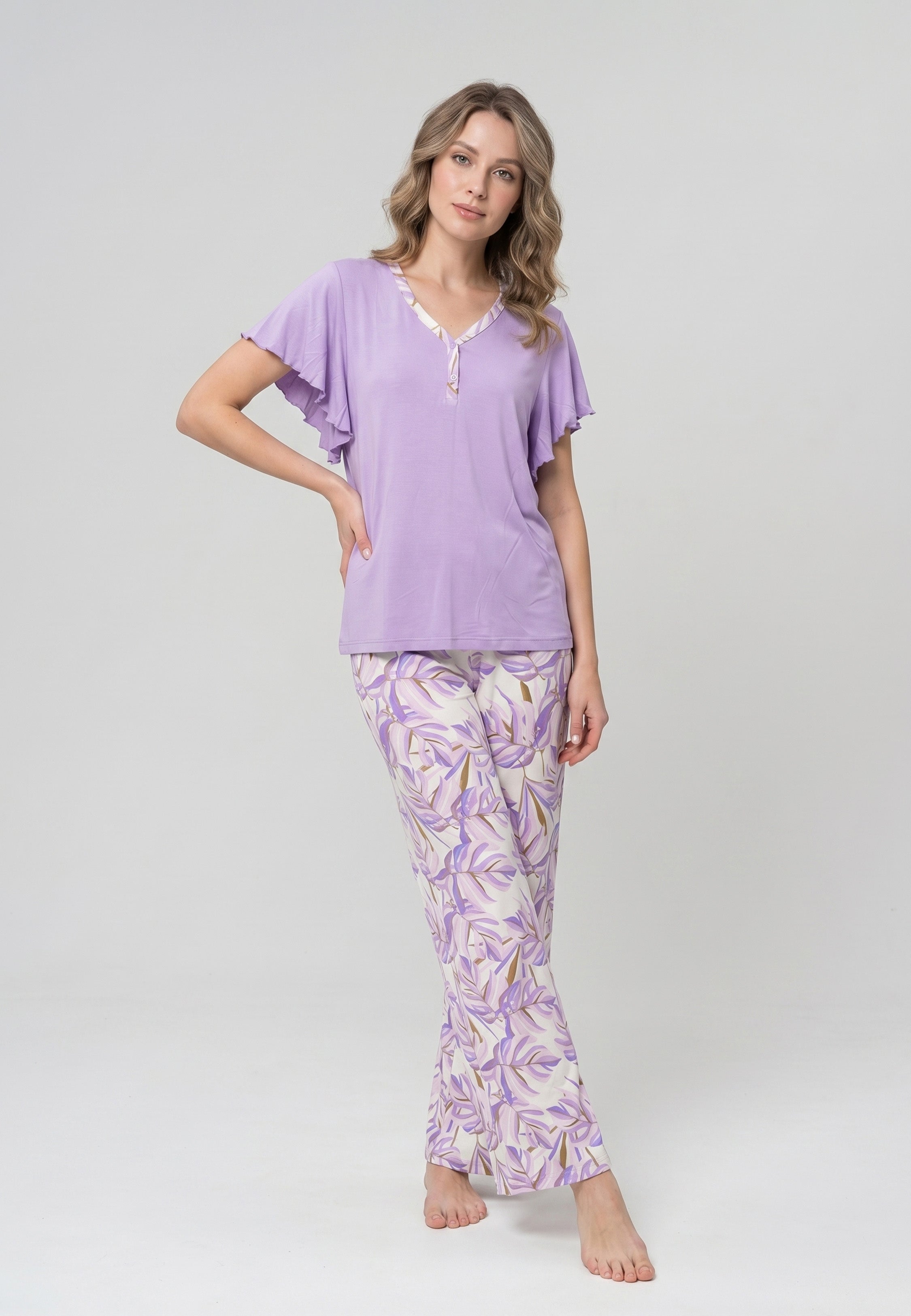 Femme portant un pyjama deux pièces haut lilas manches papillon et pantalon à imprimé feuilles tropicales violettes
