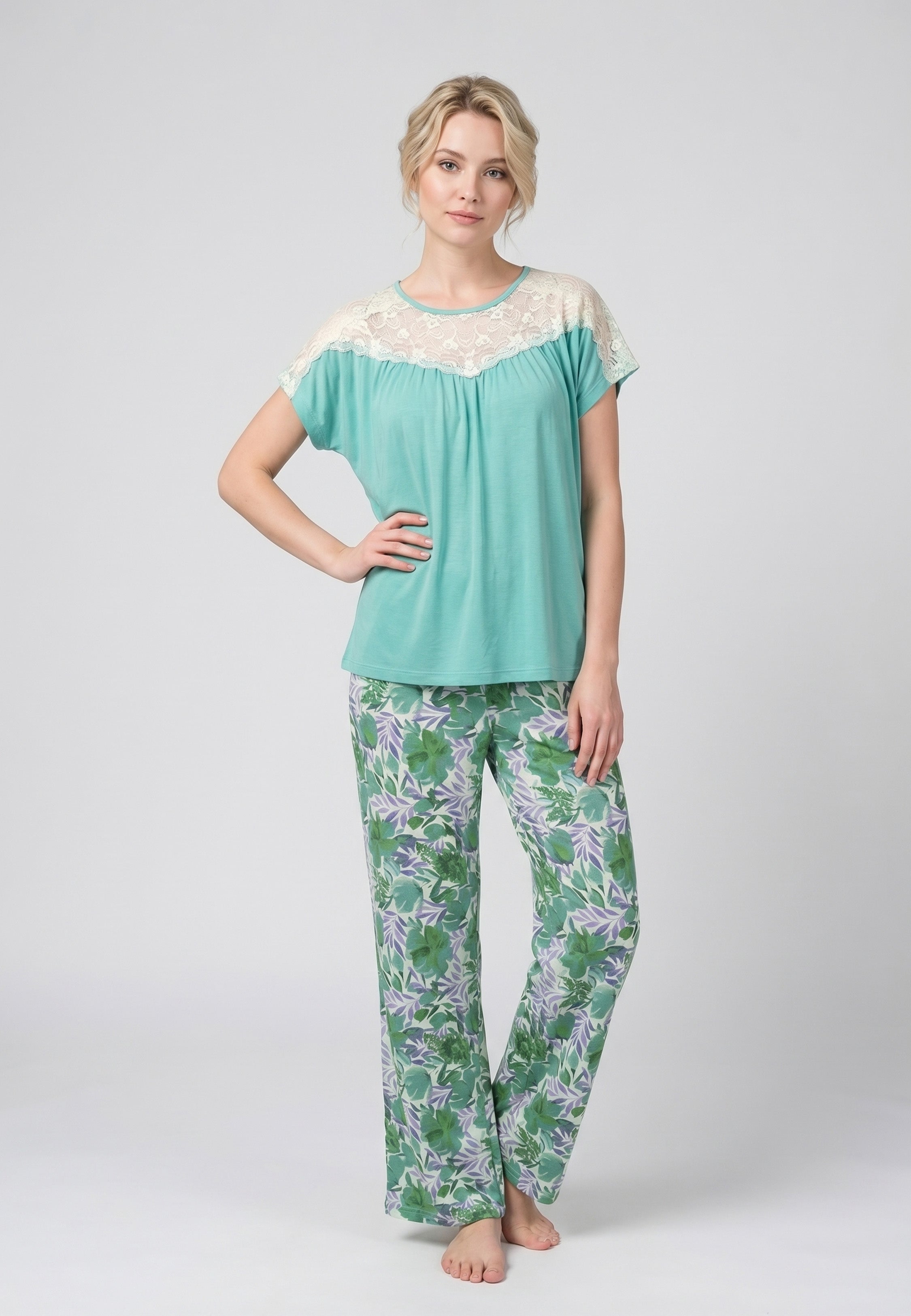 Femme portant un pyjama deux pièces haut turquoise avec empiècement dentelle crème et pantalon à imprimé feuilles tropicales vertes