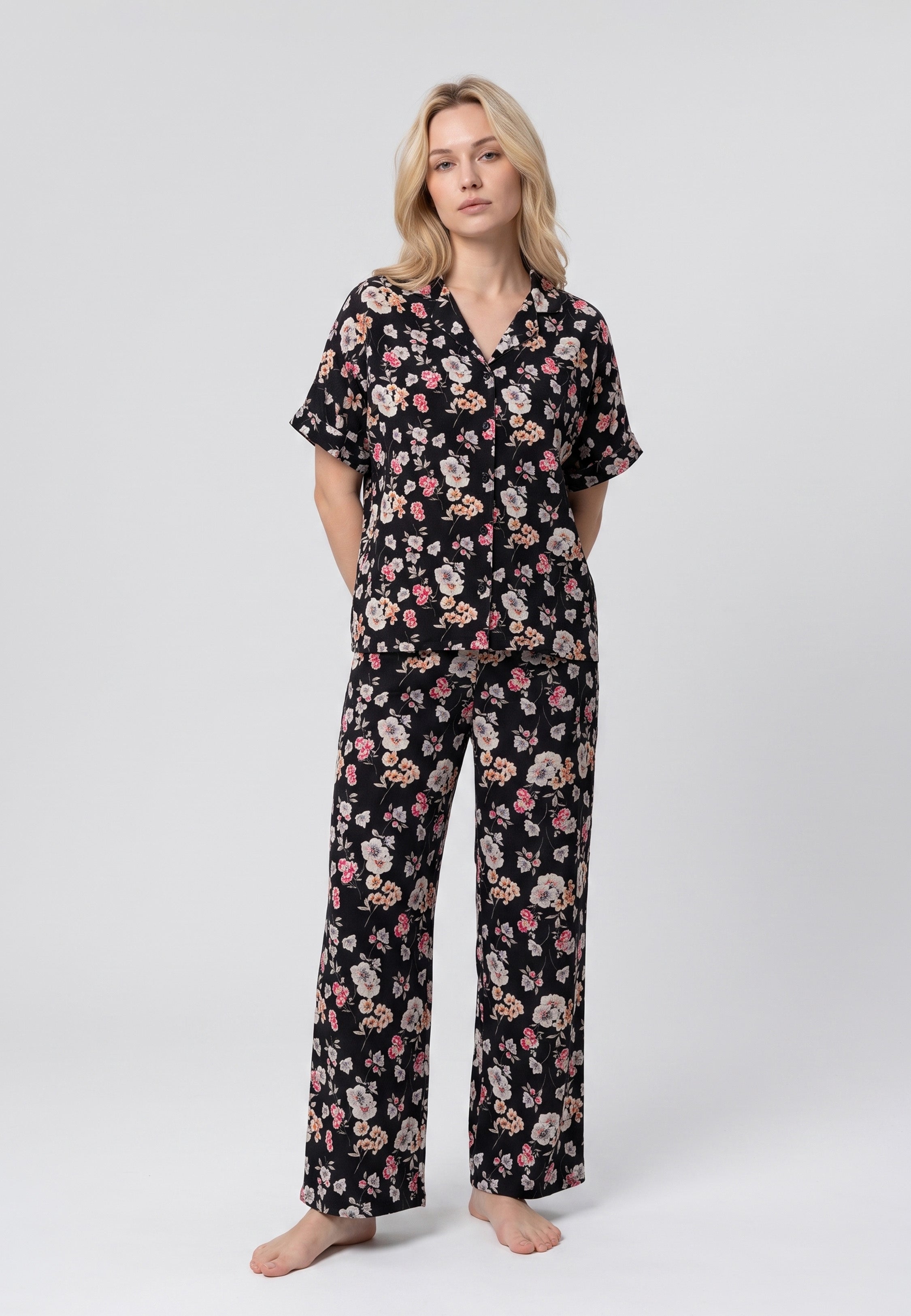 Femme portant un pyjama chemise manches courtes et pantalon large imprimé fleuri rose sur fond noir Rosabella