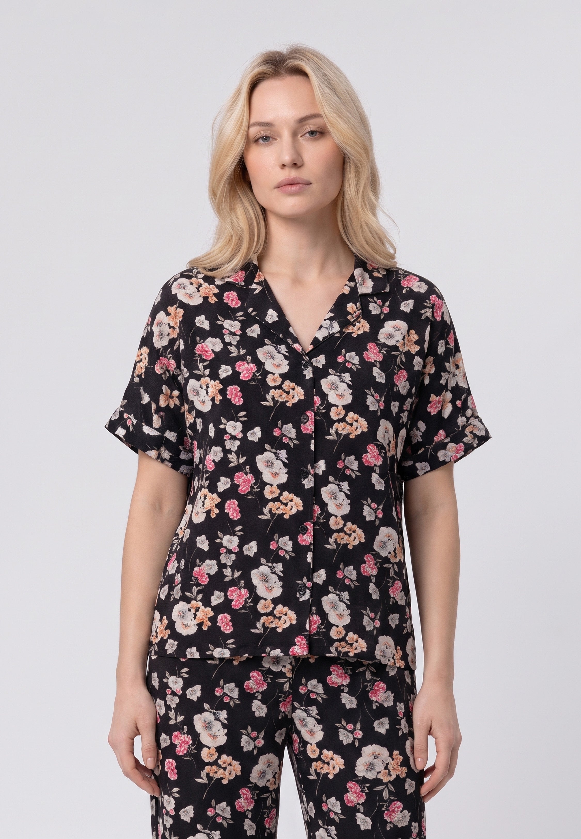 Femme portant un pyjama chemise manches courtes et pantalon large imprimé fleuri rose sur fond noir Rosabella