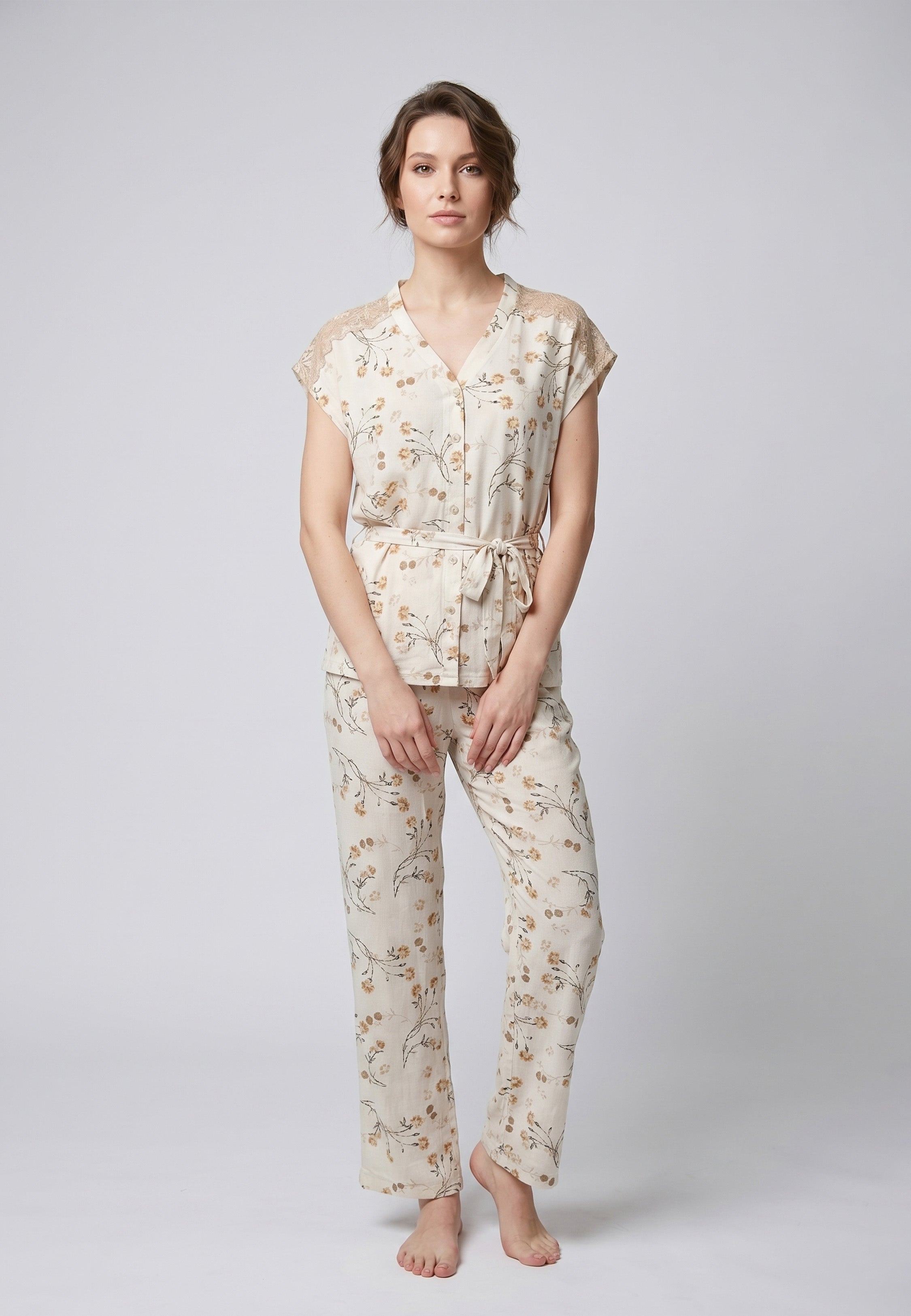 Femme portant un pyjama deux pièces blouse boutonnée col V sans manches empiècement dentelle épaules ceinture nœud imprimé fleuri beige et doré sur fond crème et pantalon droit assorti Rosabella Soft Bloom
