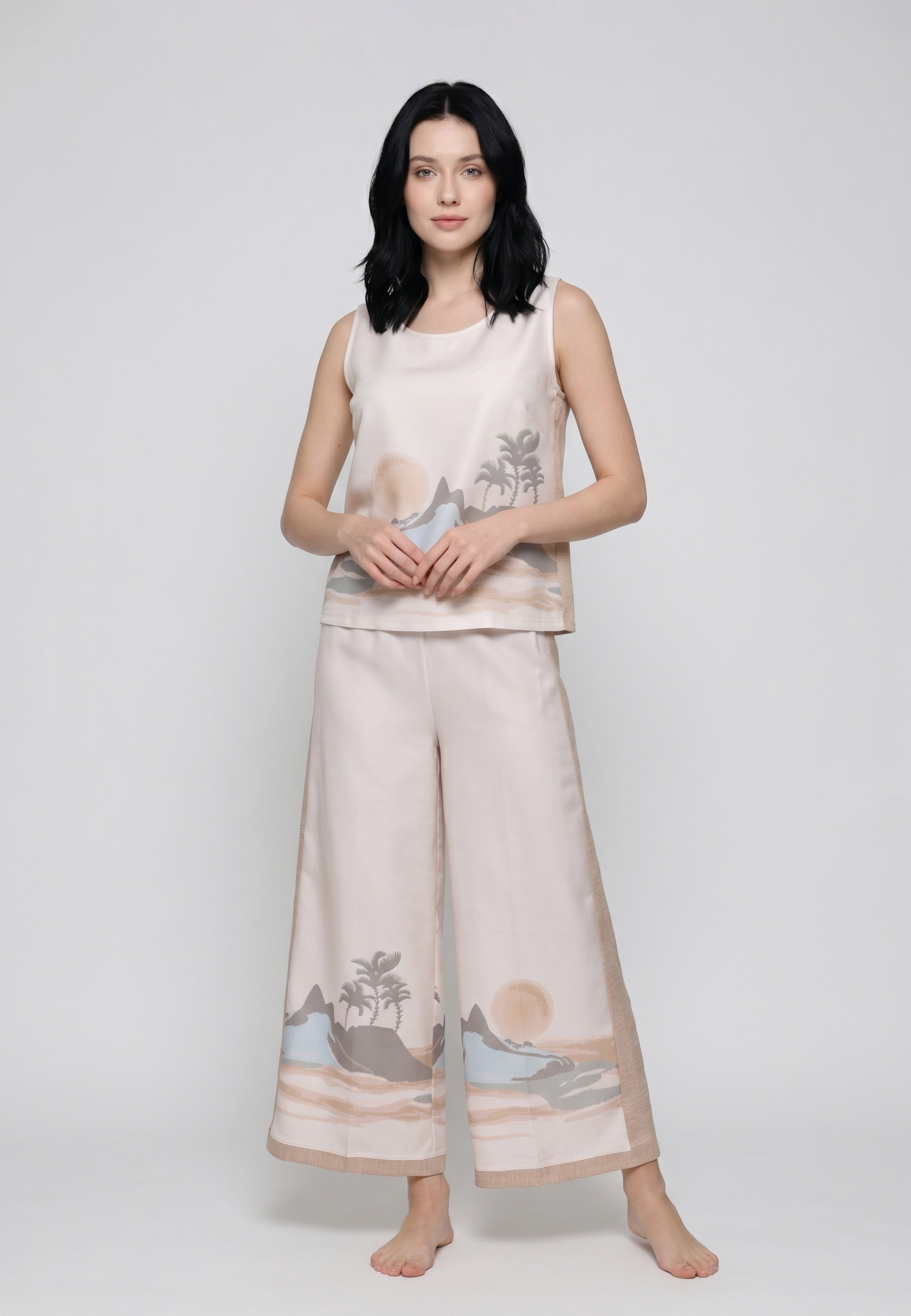 Femme portant un ensemble top sans manches et pantalon large satiné beige rosé imprimé paysage côtier tropical palmiers collines mer Rosabella