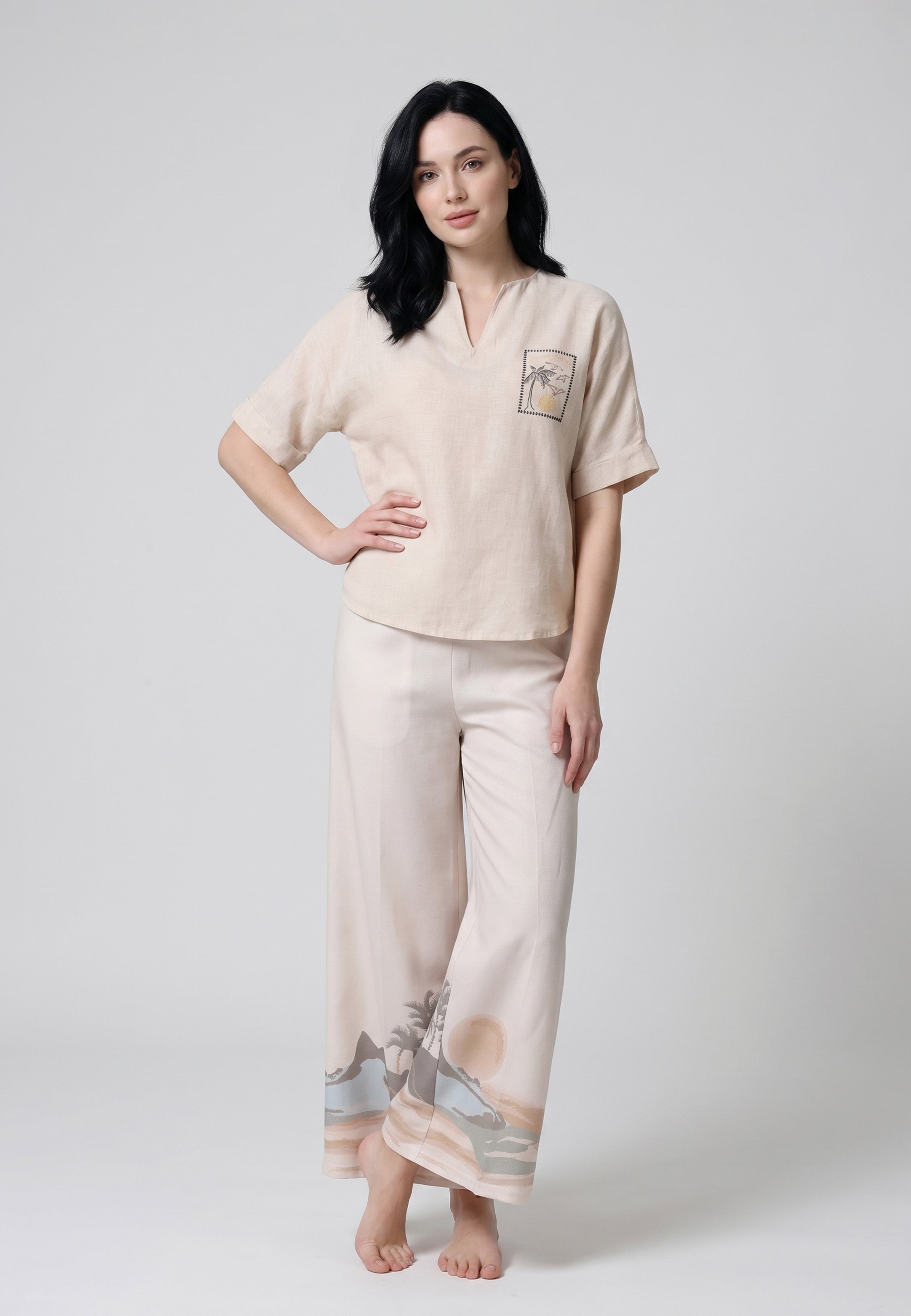 Femme portant un ensemble top tunique oversize sable patch palmier et pantalon large bordure imprimée paysage côtier palmiers soleil couchant Rosabella