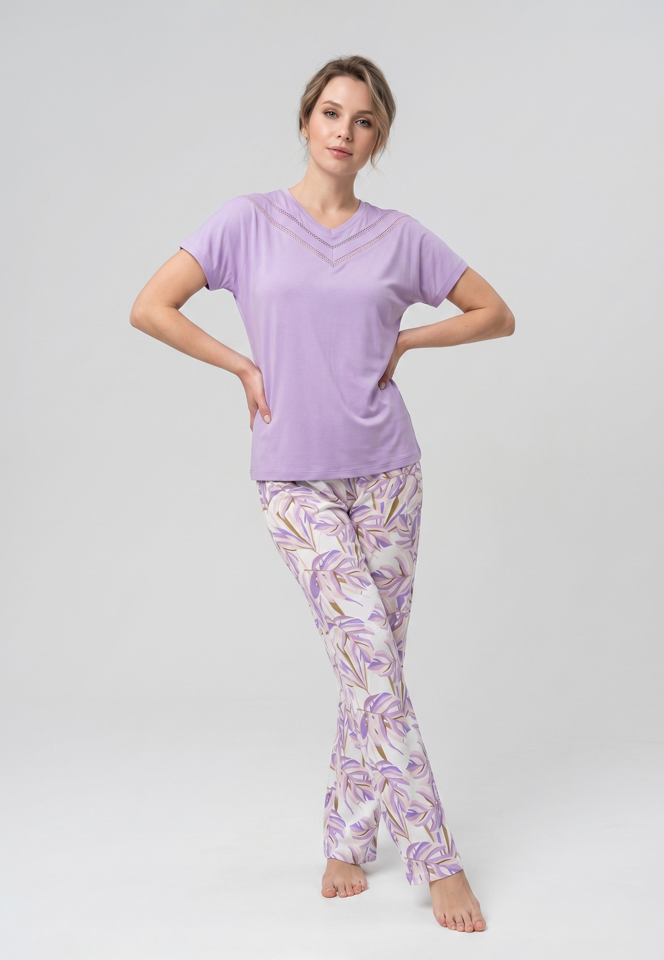 Femme portant un pyjama deux pièces t-shirt mauve clair col V dentelle et pantalon long imprimé feuillage botanique mauve et doré Rosabella Fleurs Sauvages