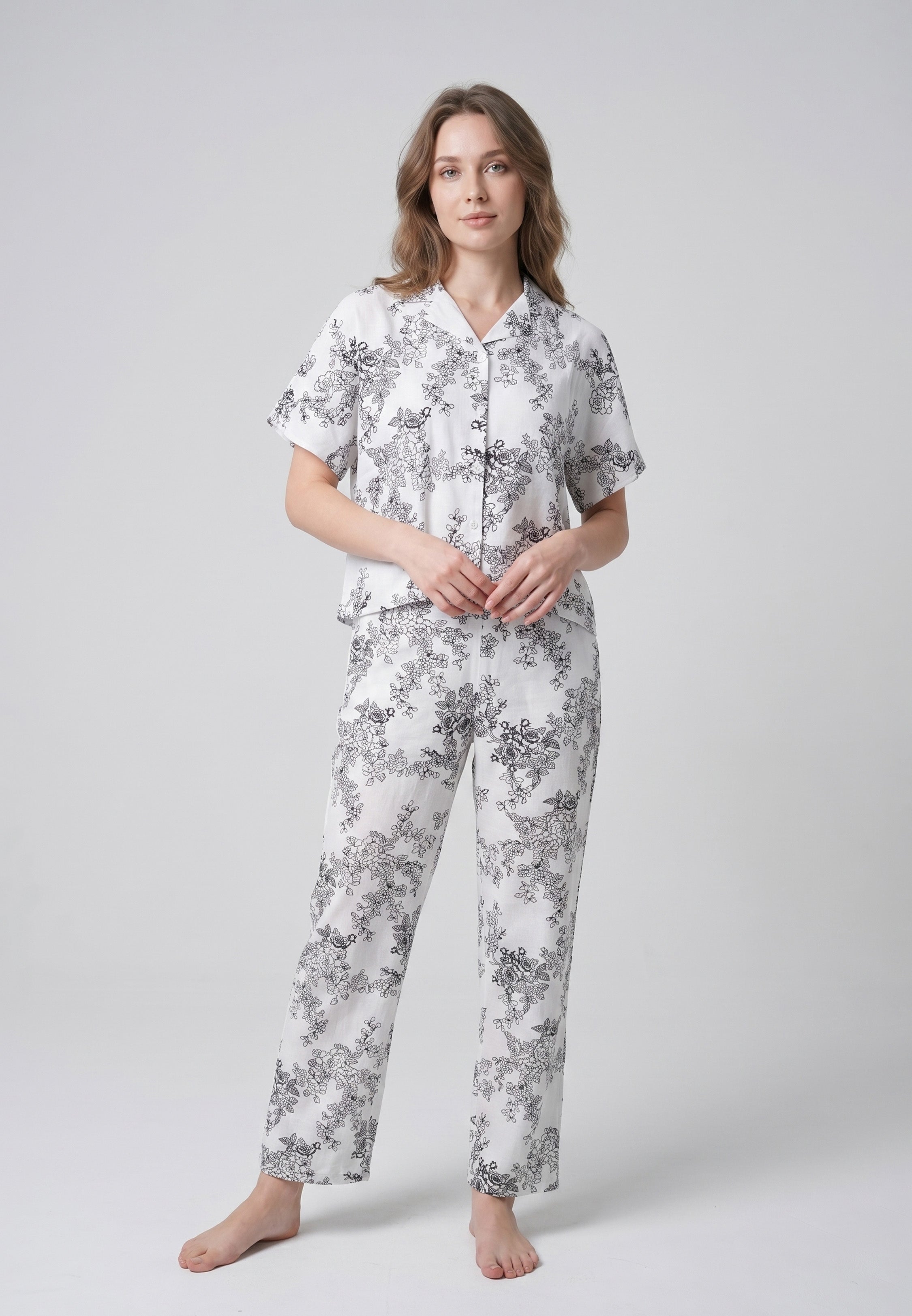 Femme portant un pyjama deux pièces chemise boutonnée col pyjama manches courtes imprimé botanique noir fond crème et pantalon droit assorti Rosabella Calm Evenings
