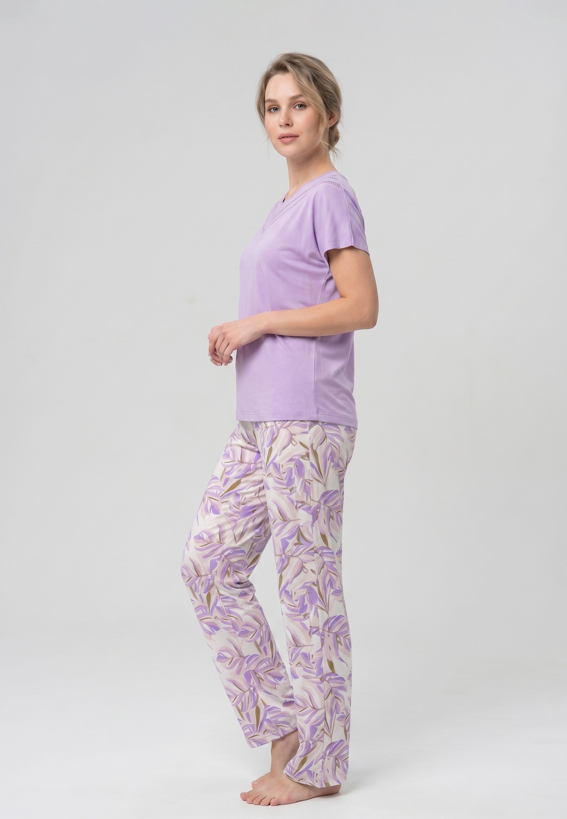 Femme portant un pyjama deux pièces t-shirt mauve clair col V dentelle et pantalon long imprimé feuillage botanique mauve et doré Rosabella Fleurs Sauvages