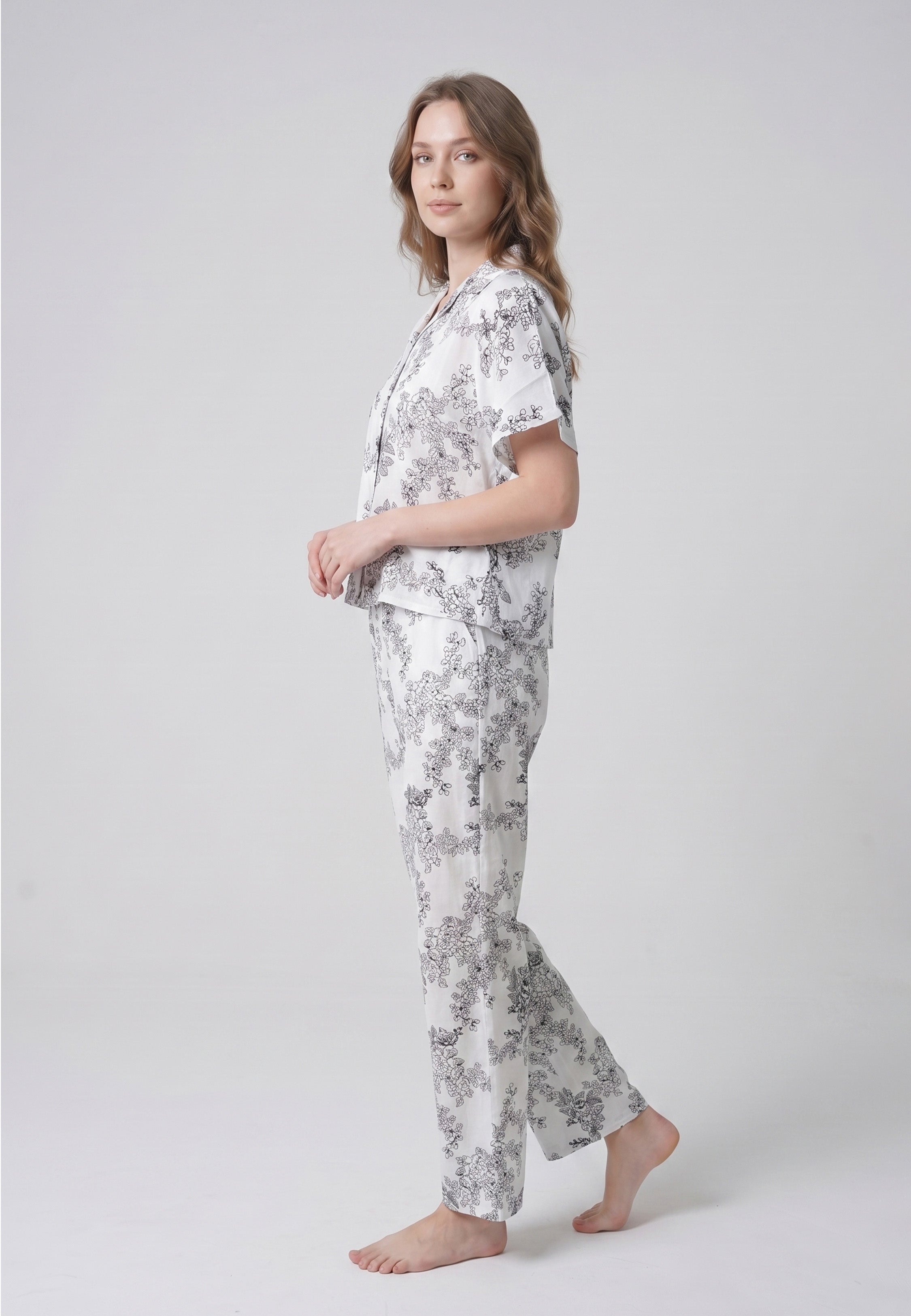 Femme portant un pyjama deux pièces chemise boutonnée col pyjama manches courtes imprimé botanique noir fond crème et pantalon droit assorti Rosabella Calm Evenings