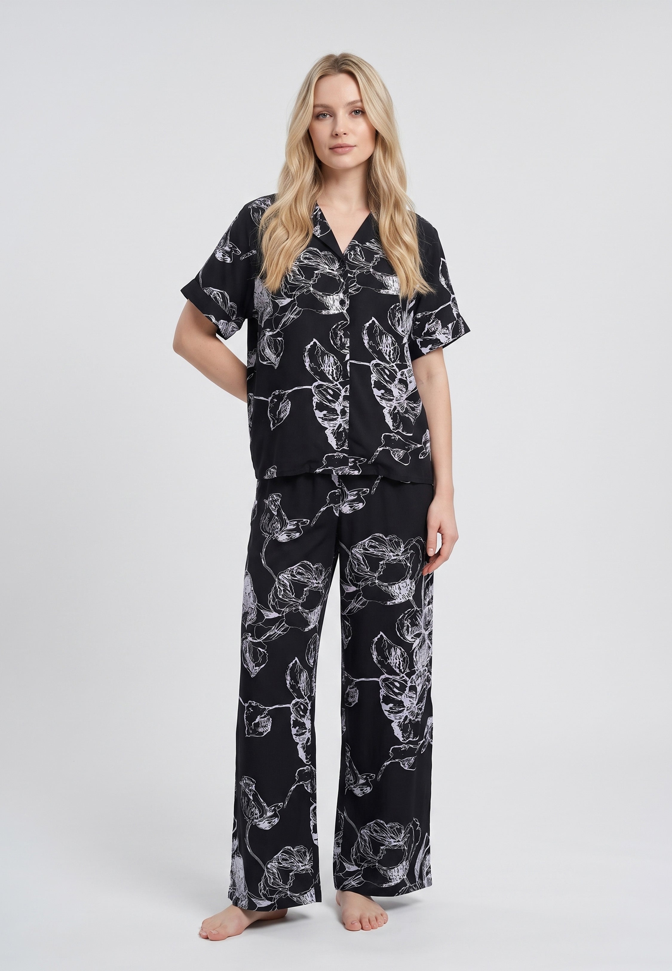 Femme portant un pyjama chemise manches courtes et pantalon large imprimé grandes fleurs écru sur fond noir Rosabella