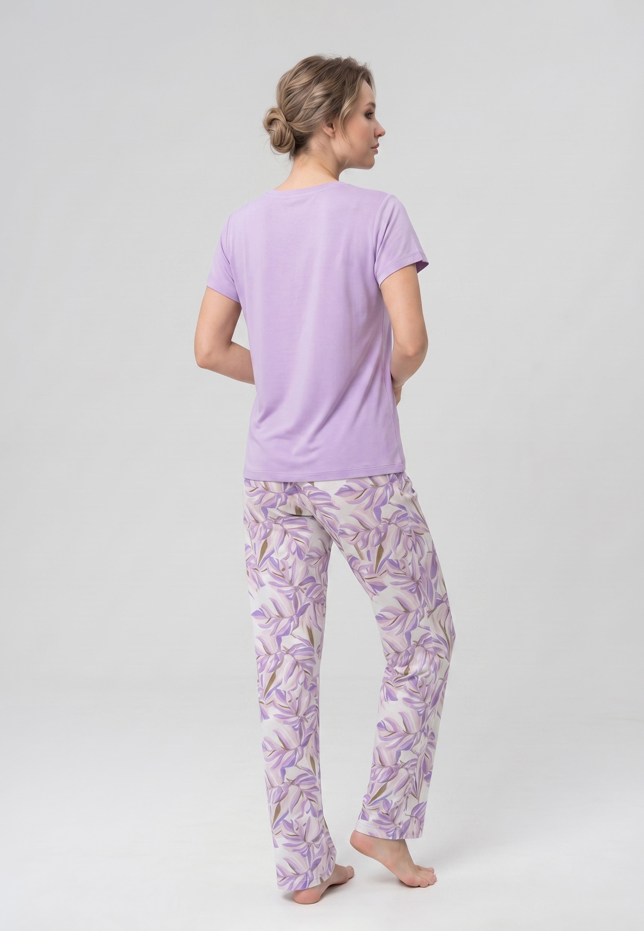 Femme portant un pyjama deux pièces t-shirt mauve clair col V dentelle et pantalon long imprimé feuillage botanique mauve et doré Rosabella Fleurs Sauvages