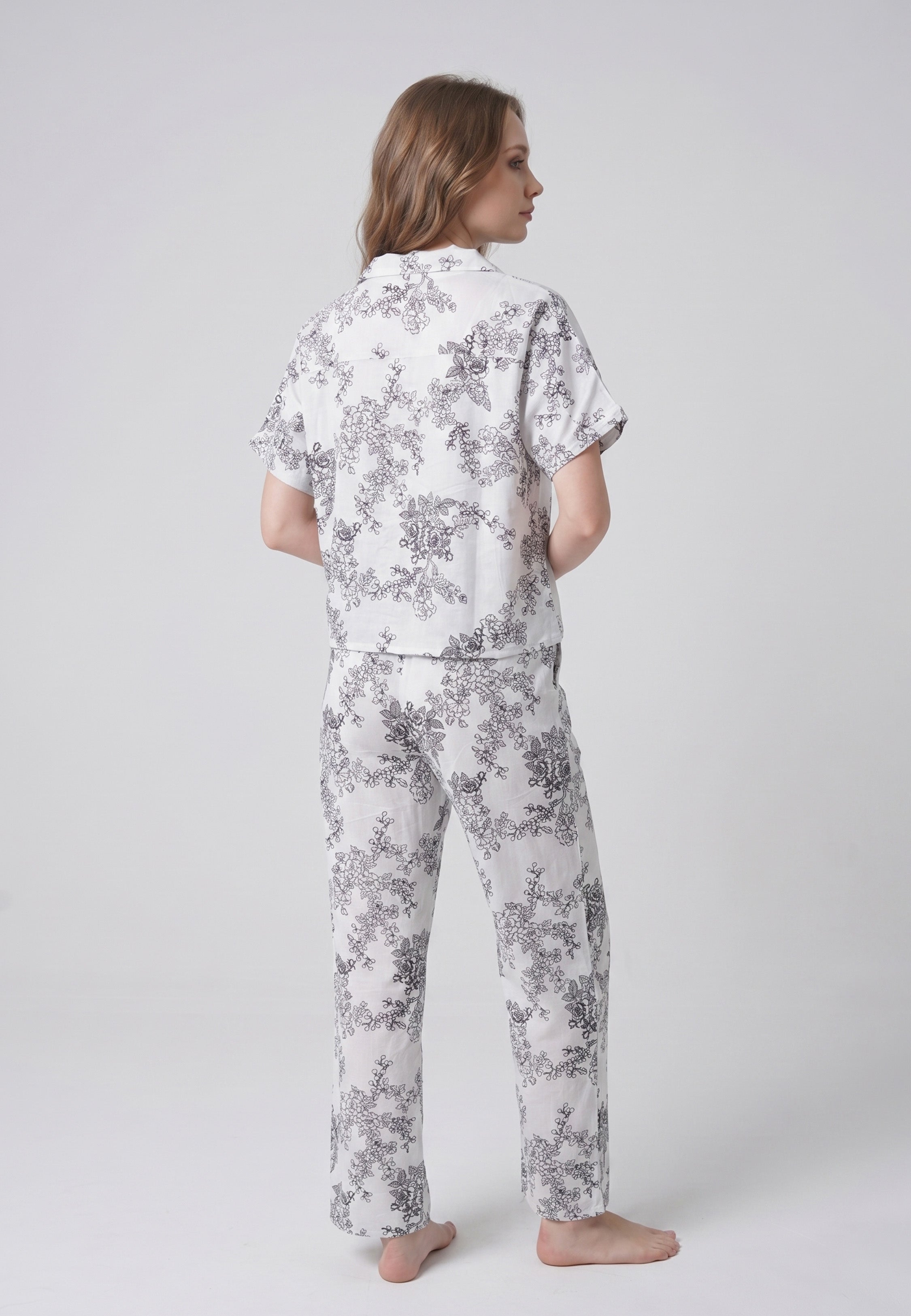 Femme portant un pyjama deux pièces chemise boutonnée col pyjama manches courtes imprimé botanique noir fond crème et pantalon droit assorti Rosabella Calm Evenings
