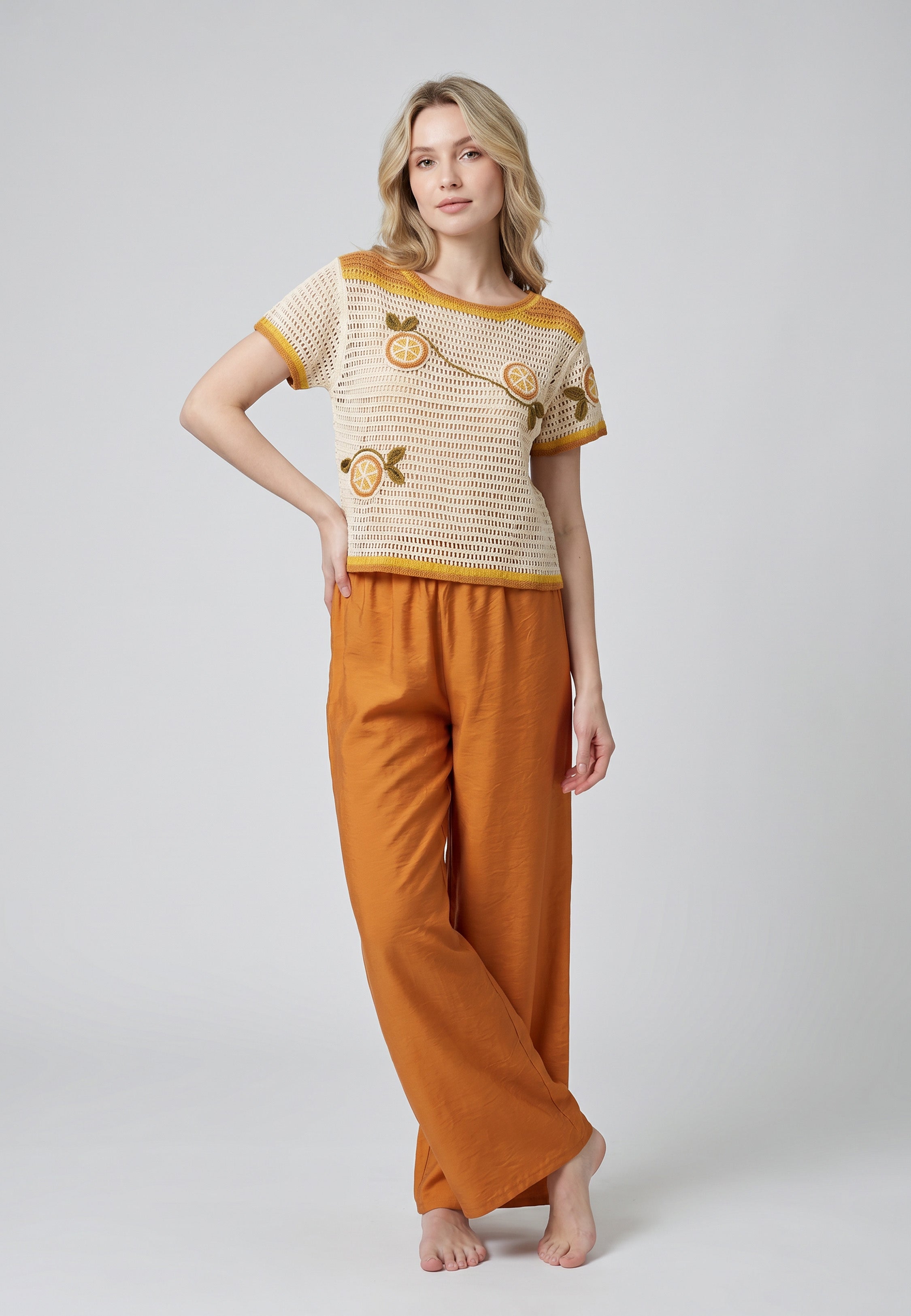 Femme portant un ensemble top crochet maille ajourée écru appliqués oranges 3D et pantalon large fluide terracotta Rosabella
