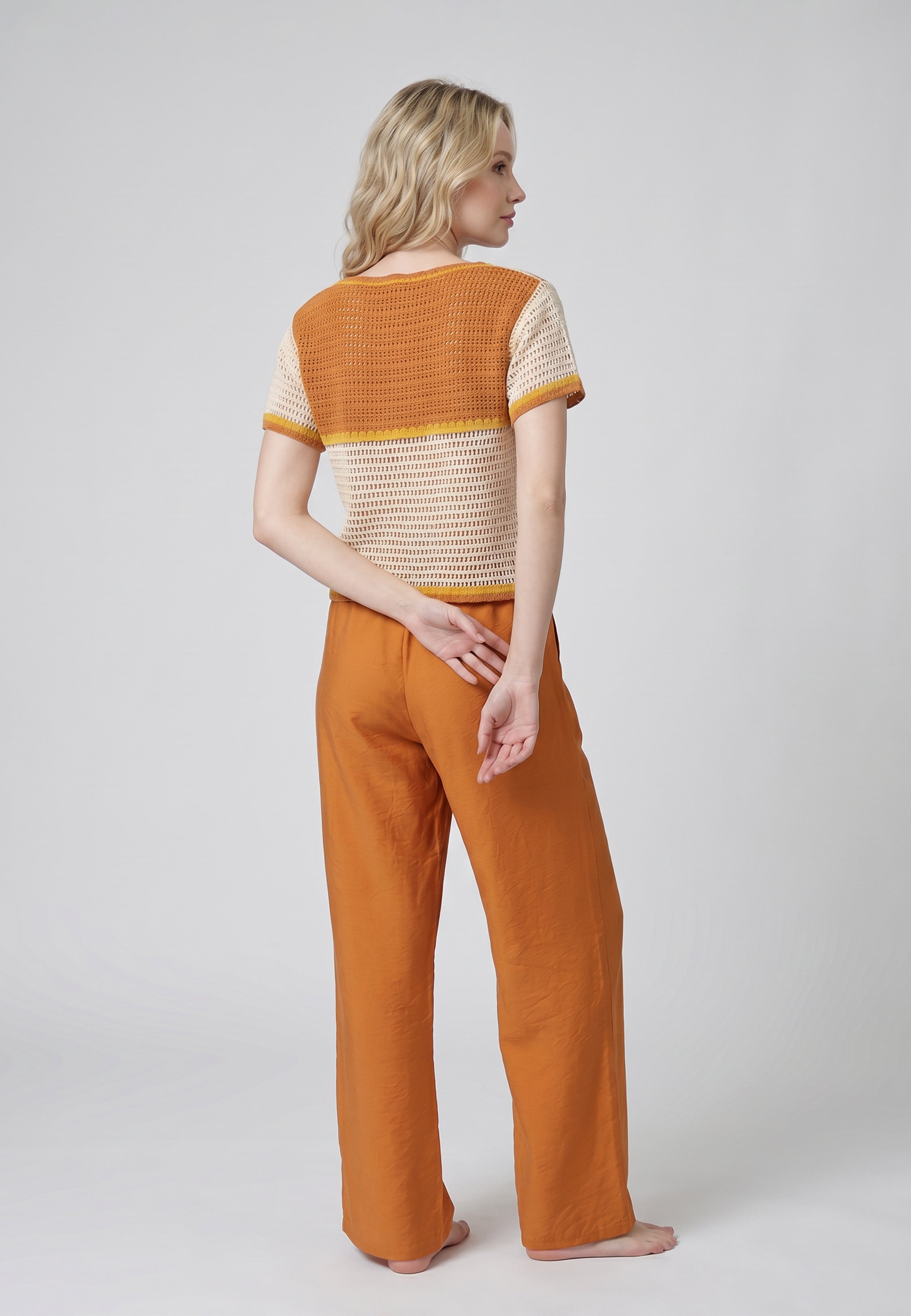 Femme portant un ensemble top crochet maille ajourée écru appliqués oranges 3D et pantalon large fluide terracotta Rosabella