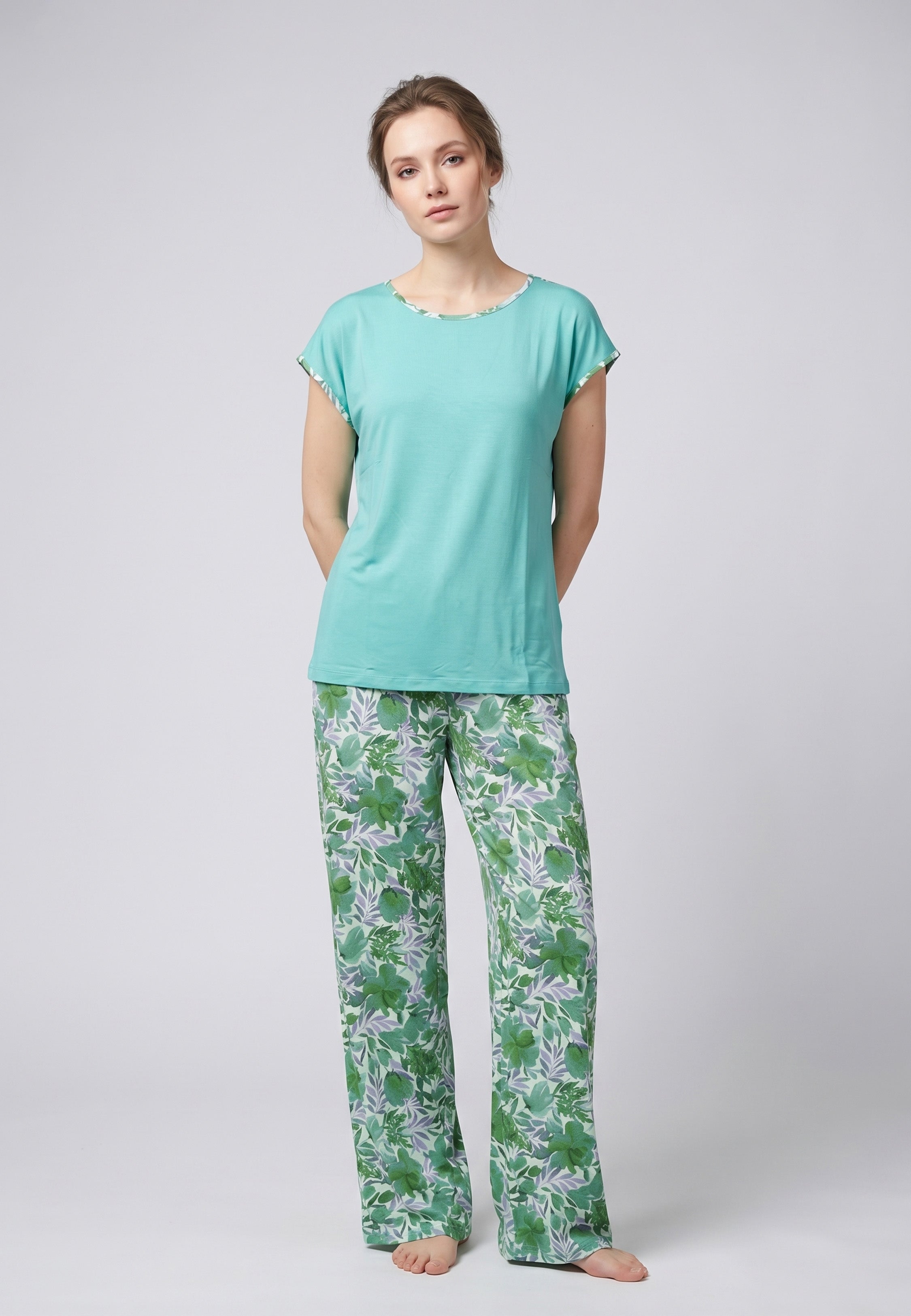Femme portant un pyjama deux pièces haut uni turquoise et pantalon à imprimé feuilles tropicales vertes