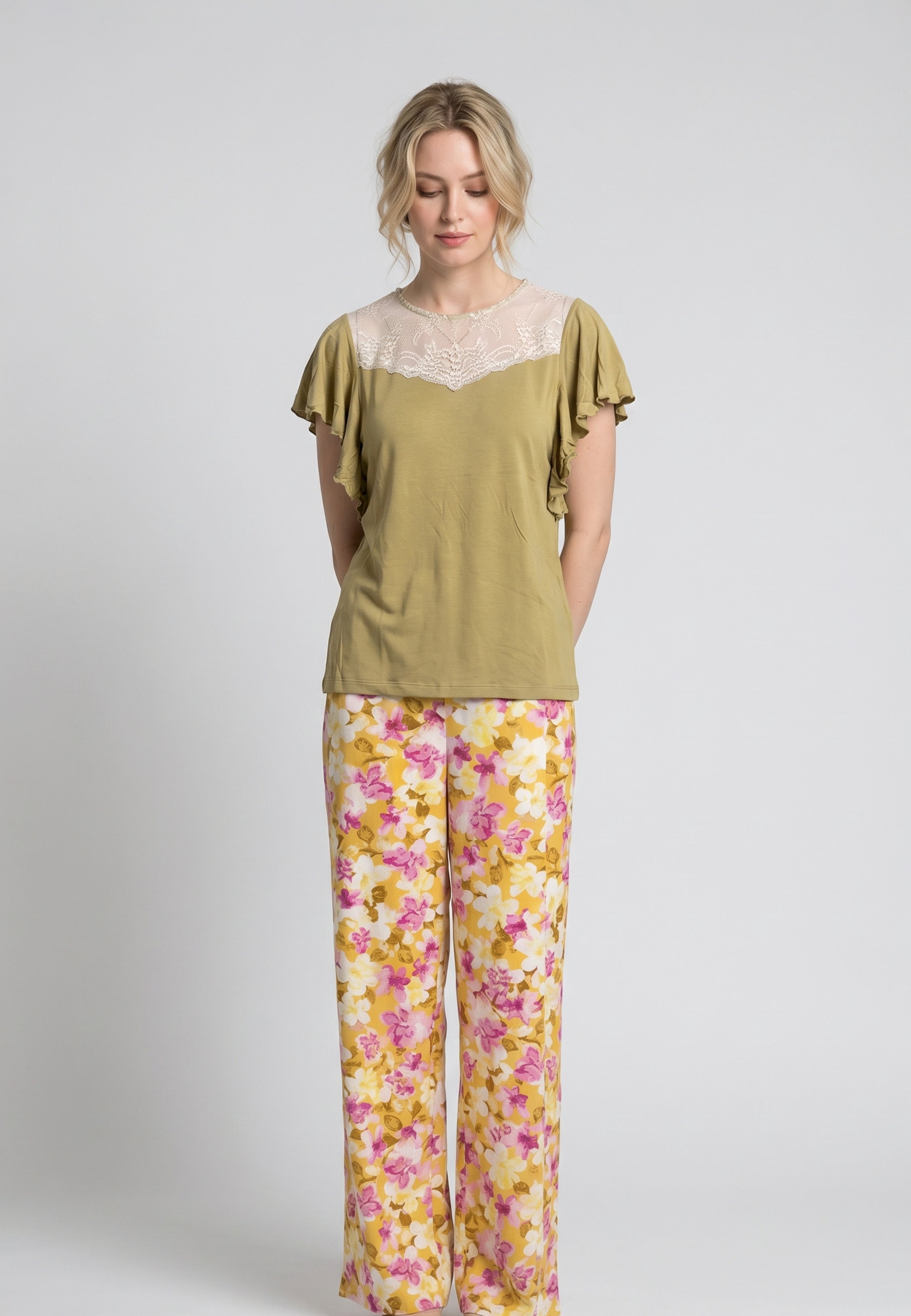 Femme portant un pyjama deux pièces haut moutarde manches volantées avec dentelle crème et pantalon à imprimé floral rose et jaune