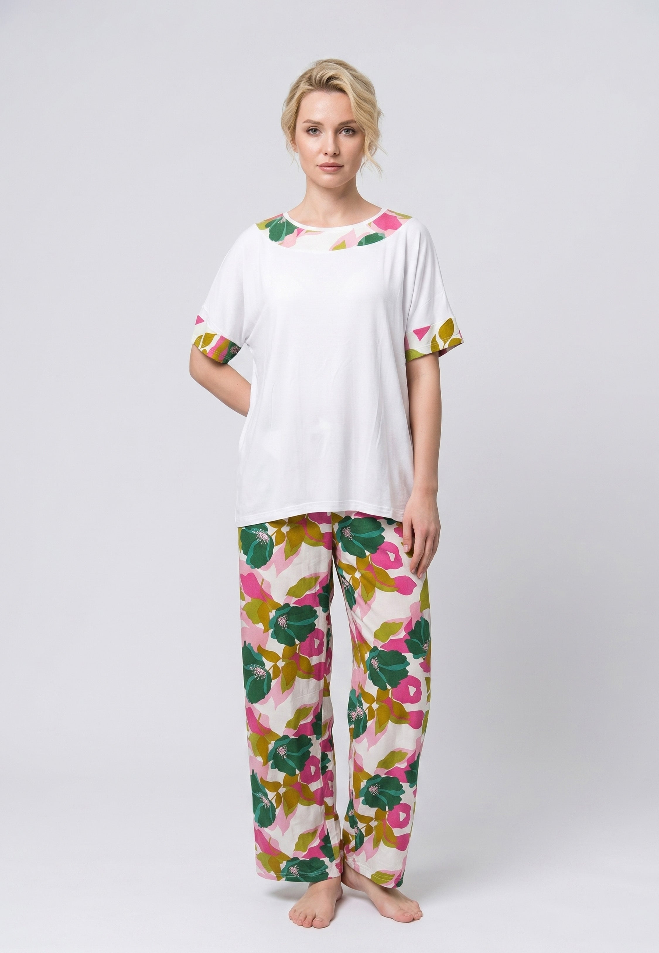Femme portant un pyjama deux pièces haut blanc oversize avec finition florale verte et rose et pantalon assorti