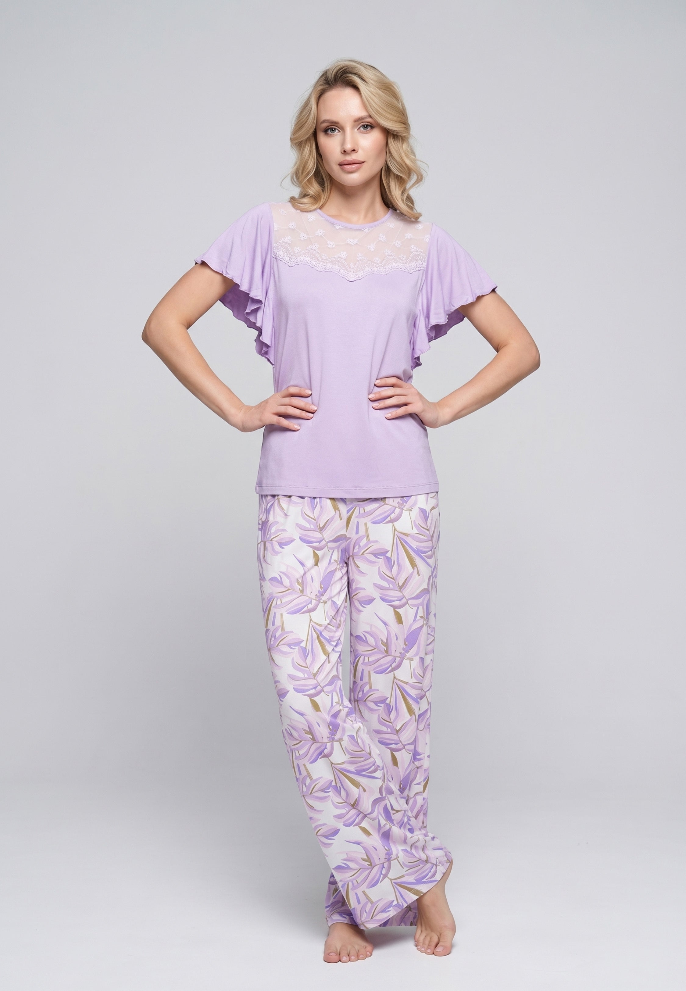 Femme portant un pyjama deux pièces haut lilas manches volantées avec dentelle crème et pantalon à imprimé feuilles mauve