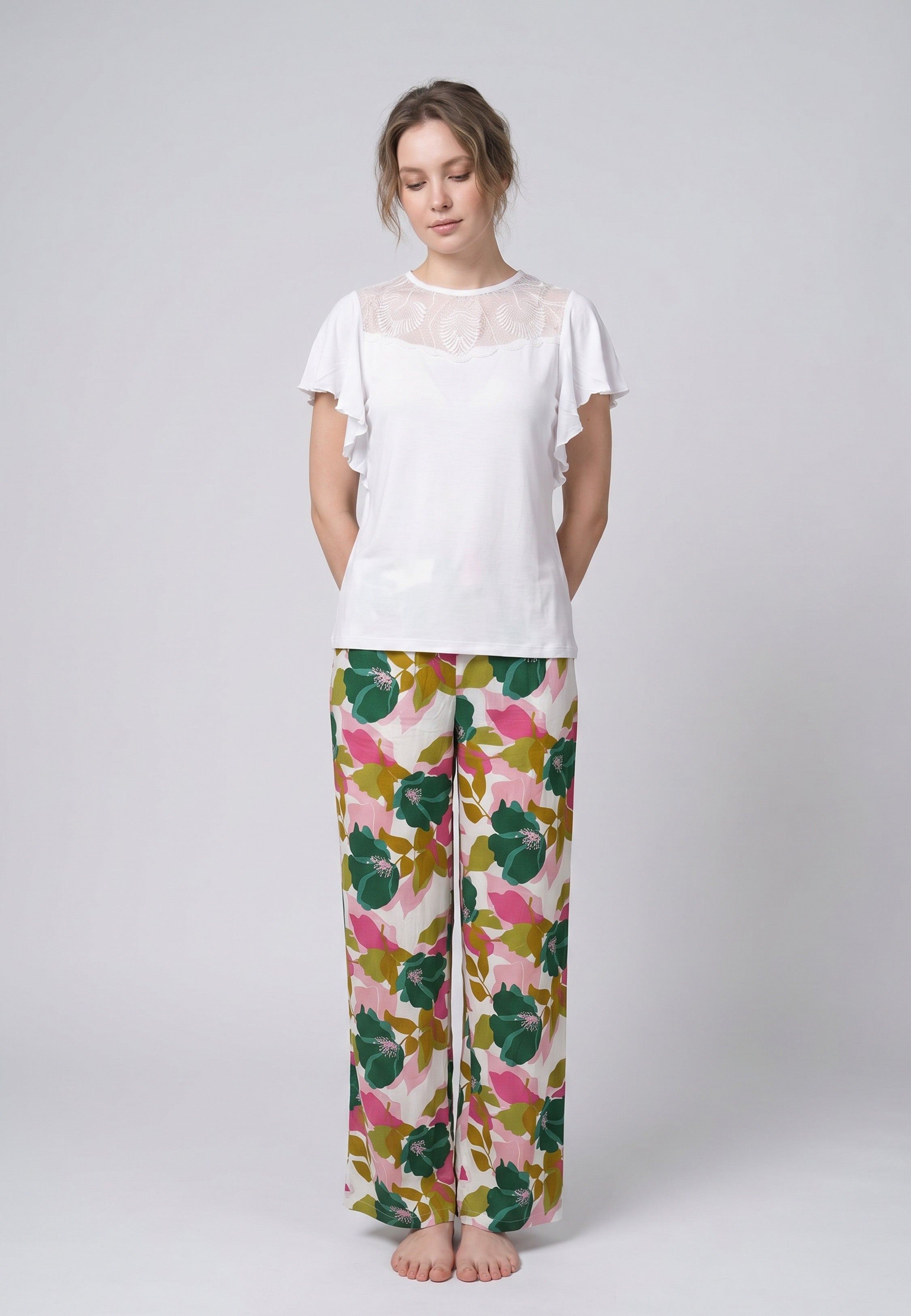 Femme portant un pyjama deux pièces haut blanc manches volantées avec dentelle et pantalon à grand imprimé floral vert et rose