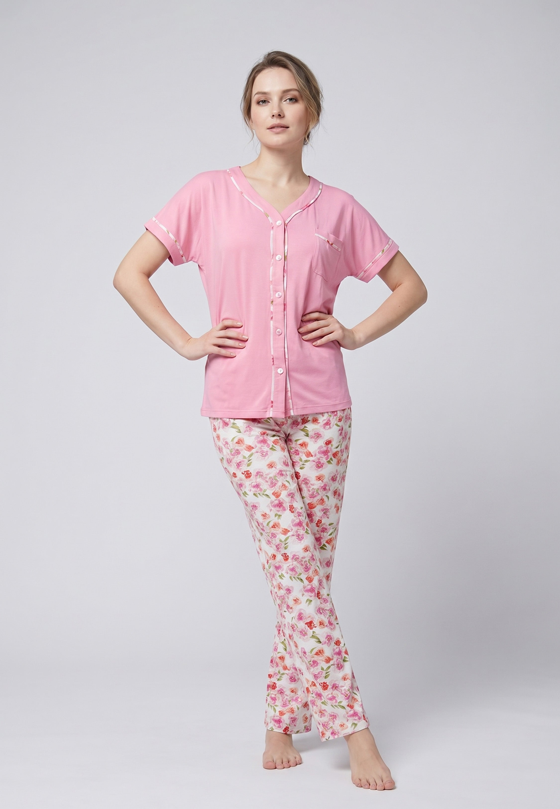 Femme portant un pyjama deux pièces chemise boutonnée manches courtes rose unie liseré fleuri et pantalon long imprimé fleuri multicolore Rosabella Floralys