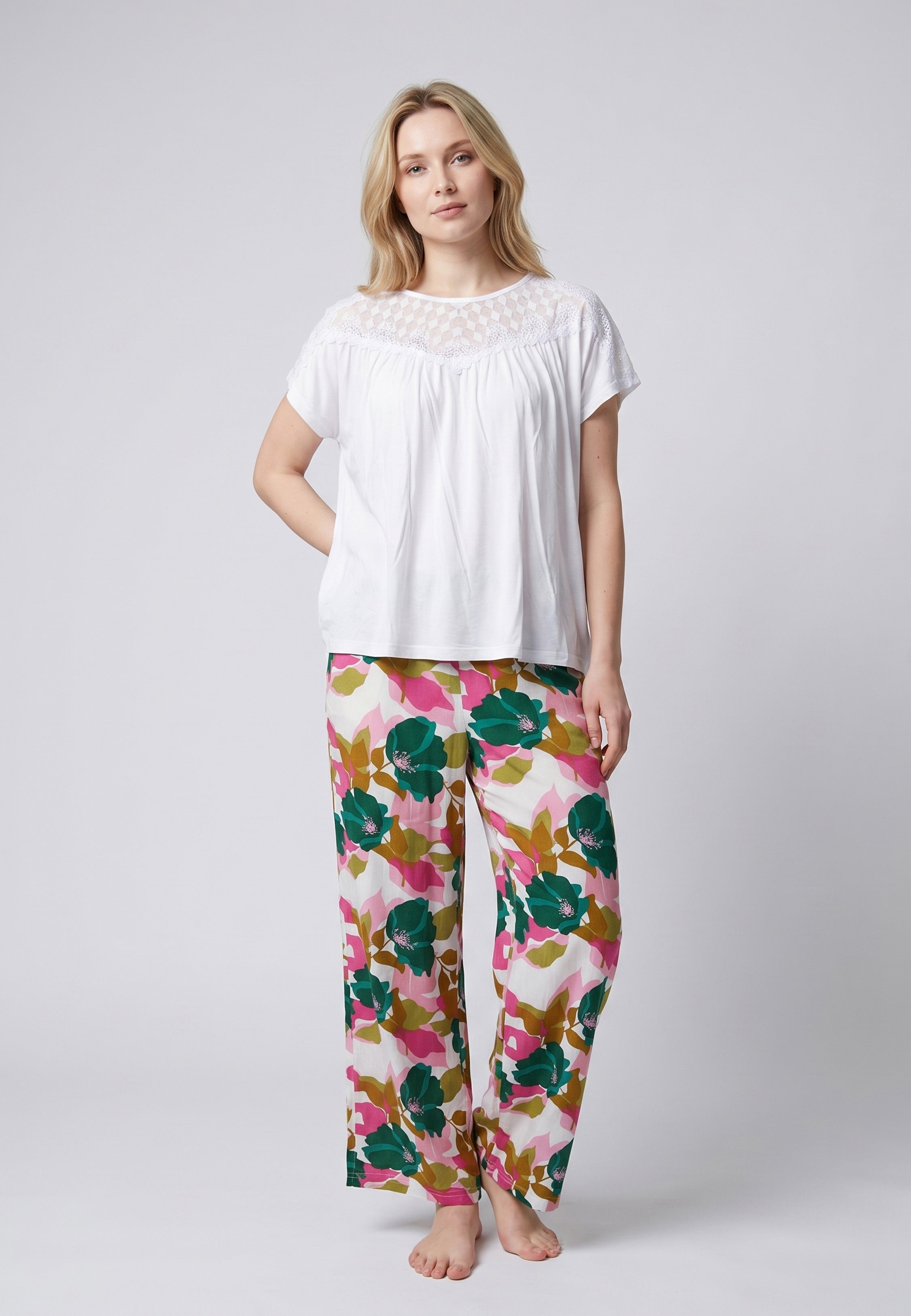 Femme portant un pyjama deux pièces haut blanc avec empiècement dentelle et pantalon à grand imprimé floral vert et rose