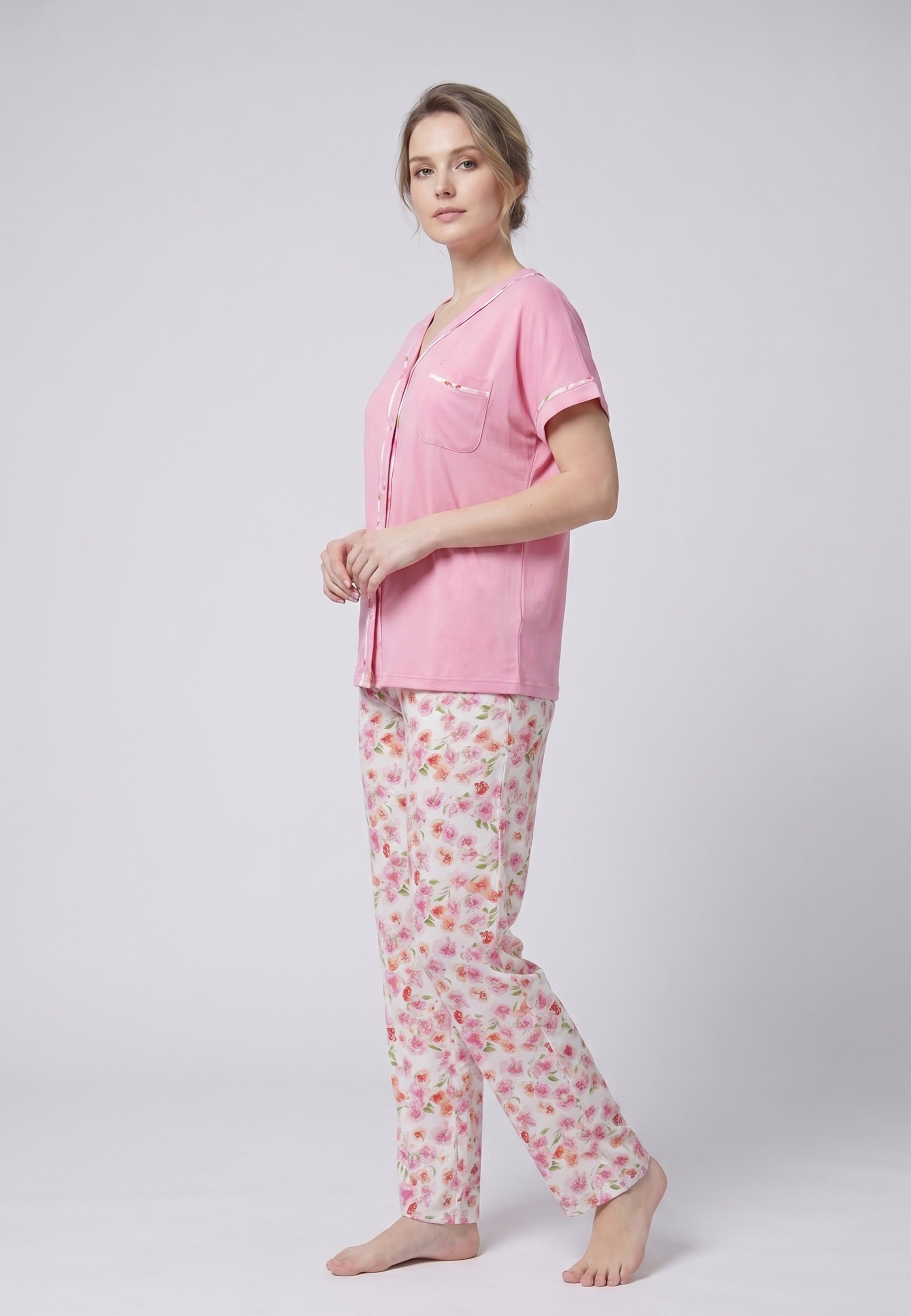 Femme portant un pyjama deux pièces chemise boutonnée manches courtes rose unie liseré fleuri et pantalon long imprimé fleuri multicolore Rosabella Floralys
