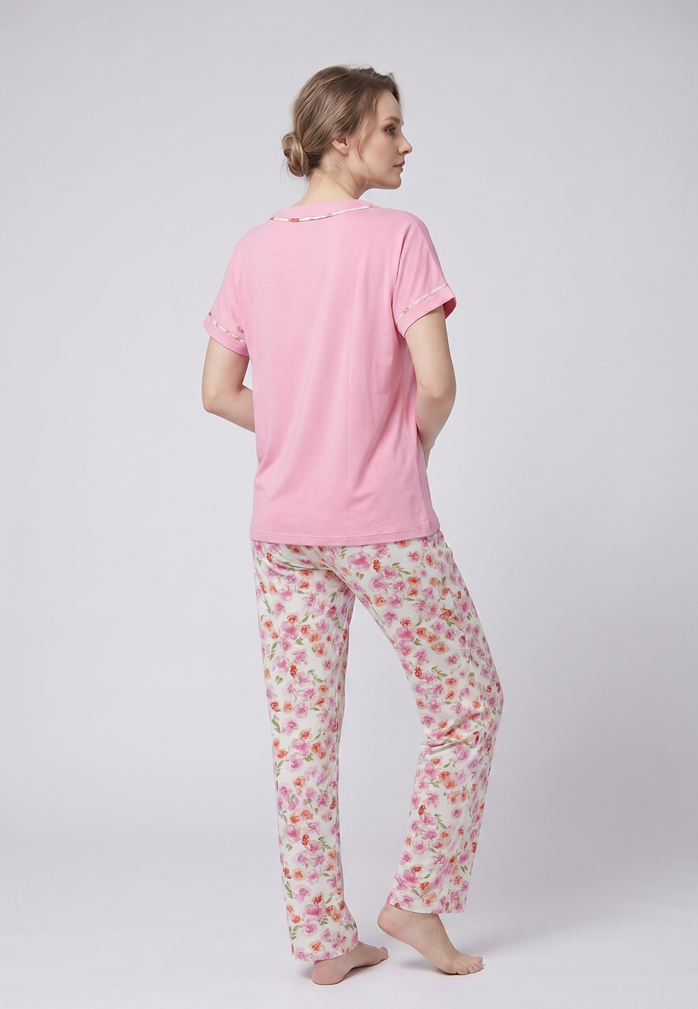 Femme portant un pyjama deux pièces chemise boutonnée manches courtes rose unie liseré fleuri et pantalon long imprimé fleuri multicolore Rosabella Floralys