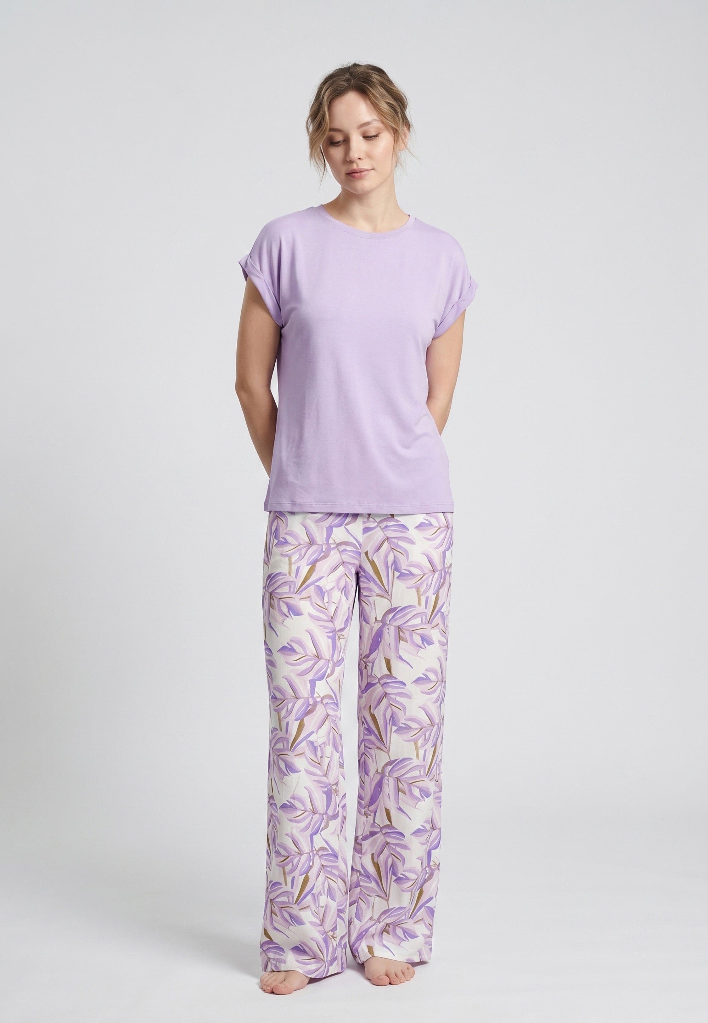 Femme portant un pyjama deux pièces haut uni violet et pantalon à imprimé feuilles tropicales lilas et doré