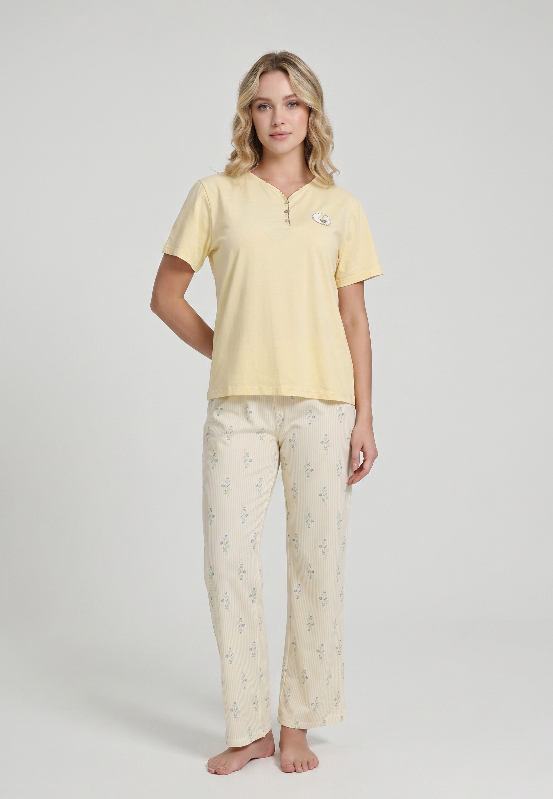 Femme portant un pyjama deux pièces top col V boutonné manches courtes uni jaune pâle badge fleuri brodé et pantalon droit rayé fleuri crème et jaune Rosabella Flowers Scent