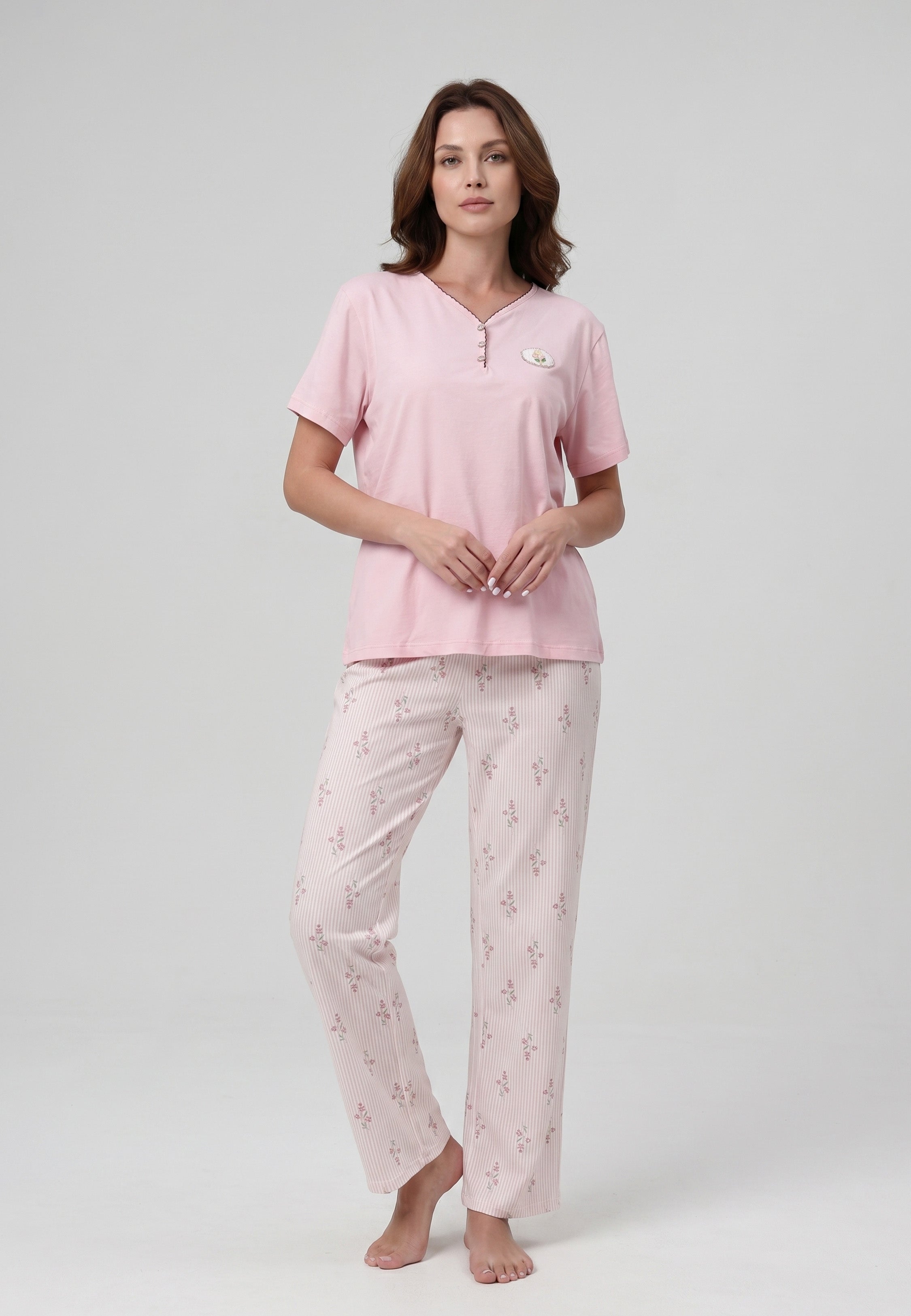 Femme portant un pyjama deux pièces top col V boutonné manches courtes uni rose badge fleuri brodé et pantalon droit rayé fleuri rose et blanc Rosabella Flowers Scent