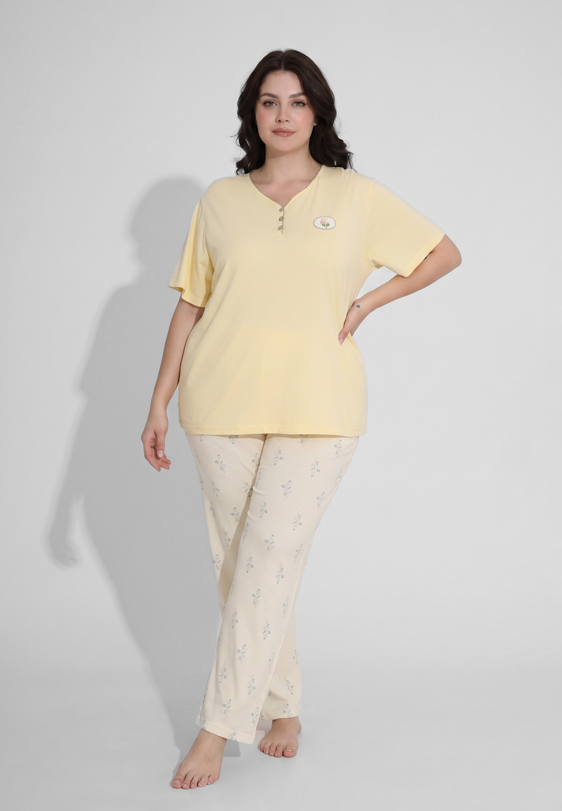 Femme portant un pyjama grande taille top col V boutonné manches courtes uni jaune pâle badge fleuri brodé et pantalon droit rayé fleuri crème et jaune Rosabella Flowers Scent