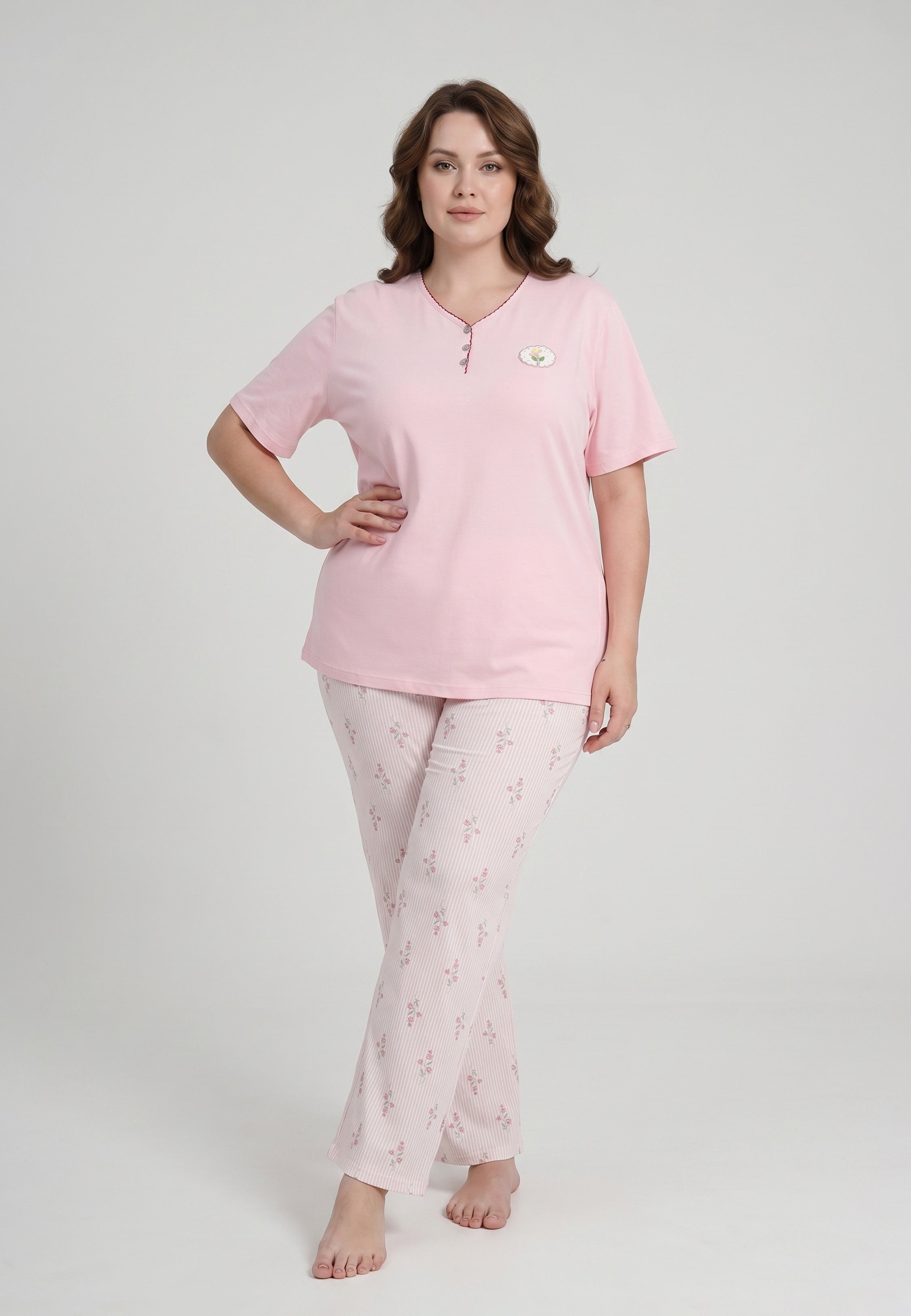 Femme portant un pyjama grande taille top col V boutonné manches courtes uni rose badge fleuri brodé et pantalon droit rayé fleuri rose et blanc Rosabella Flowers Scent