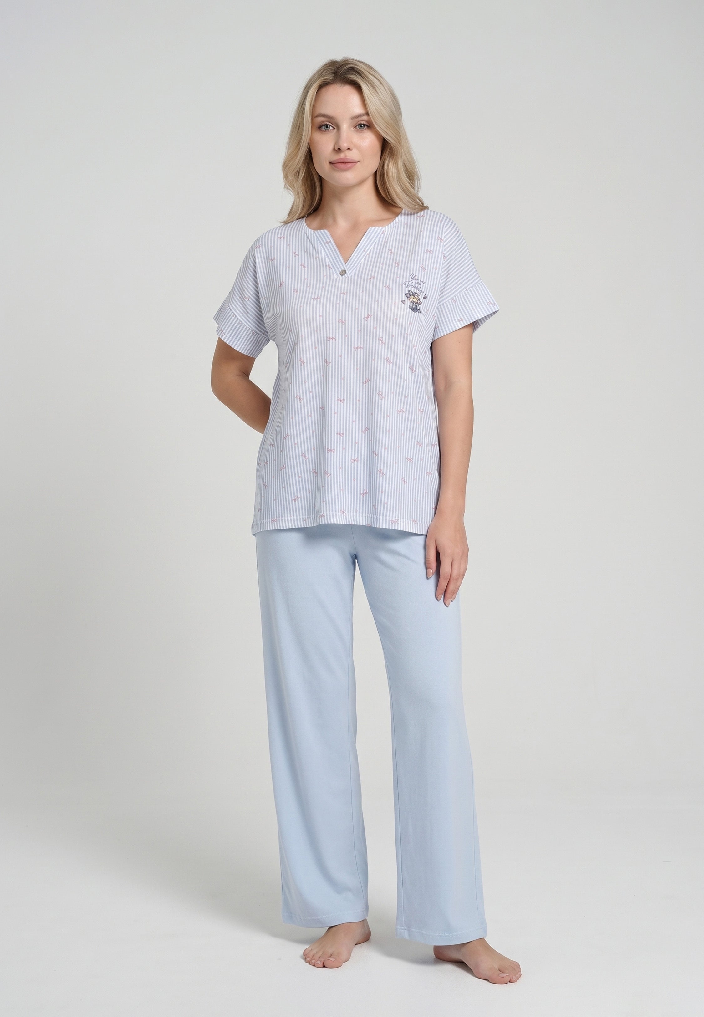 Femme portant un pyjama deux pièces top col V boutonné manches courtes imprimé rayé fleuri bleu ciel et blanc badge brodé et pantalon large uni bleu ciel Rosabella Lina