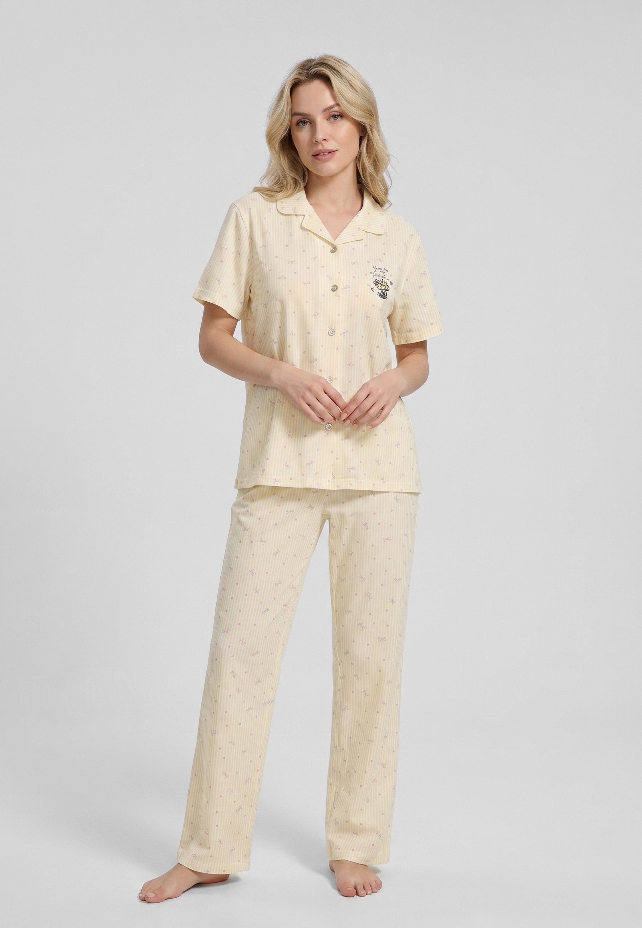 Femme portant un pyjama deux pièces chemise boutonnée col pyjama à revers manches courtes imprimé rayé fleuri jaune et blanc badge brodé et pantalon droit assorti Rosabella Lina