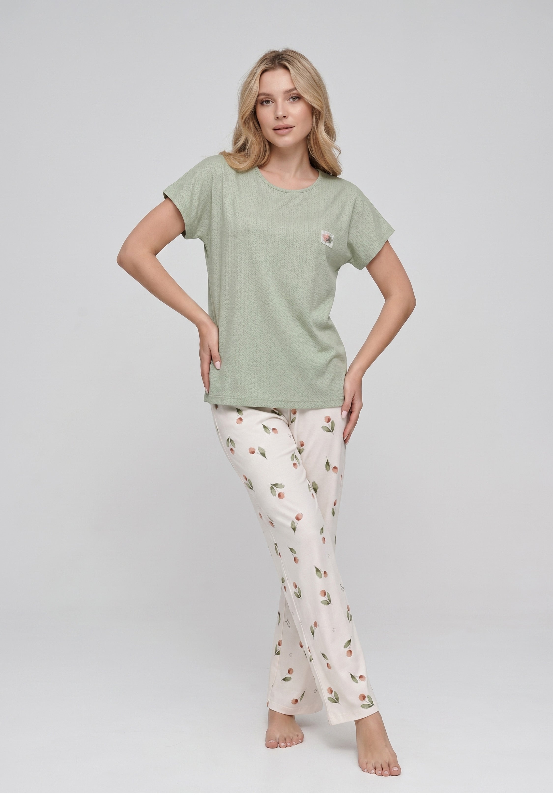 Femme portant un pyjama top col rond manches courtes texturé uni kaki badge brodé et pantalon large imprimé cerises et pêches aquarelle fond crème Rosabella Douceur Cerise