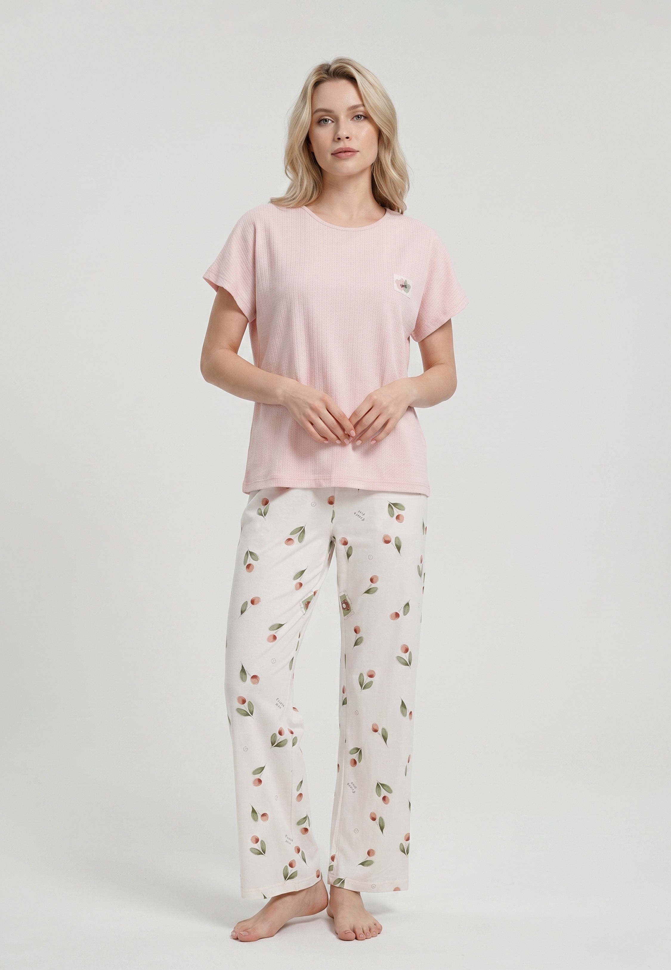 Femme portant un pyjama top col rond manches courtes texturé uni rose badge brodé et pantalon large imprimé cerises et pêches aquarelle fond crème Rosabella Douceur Cerise