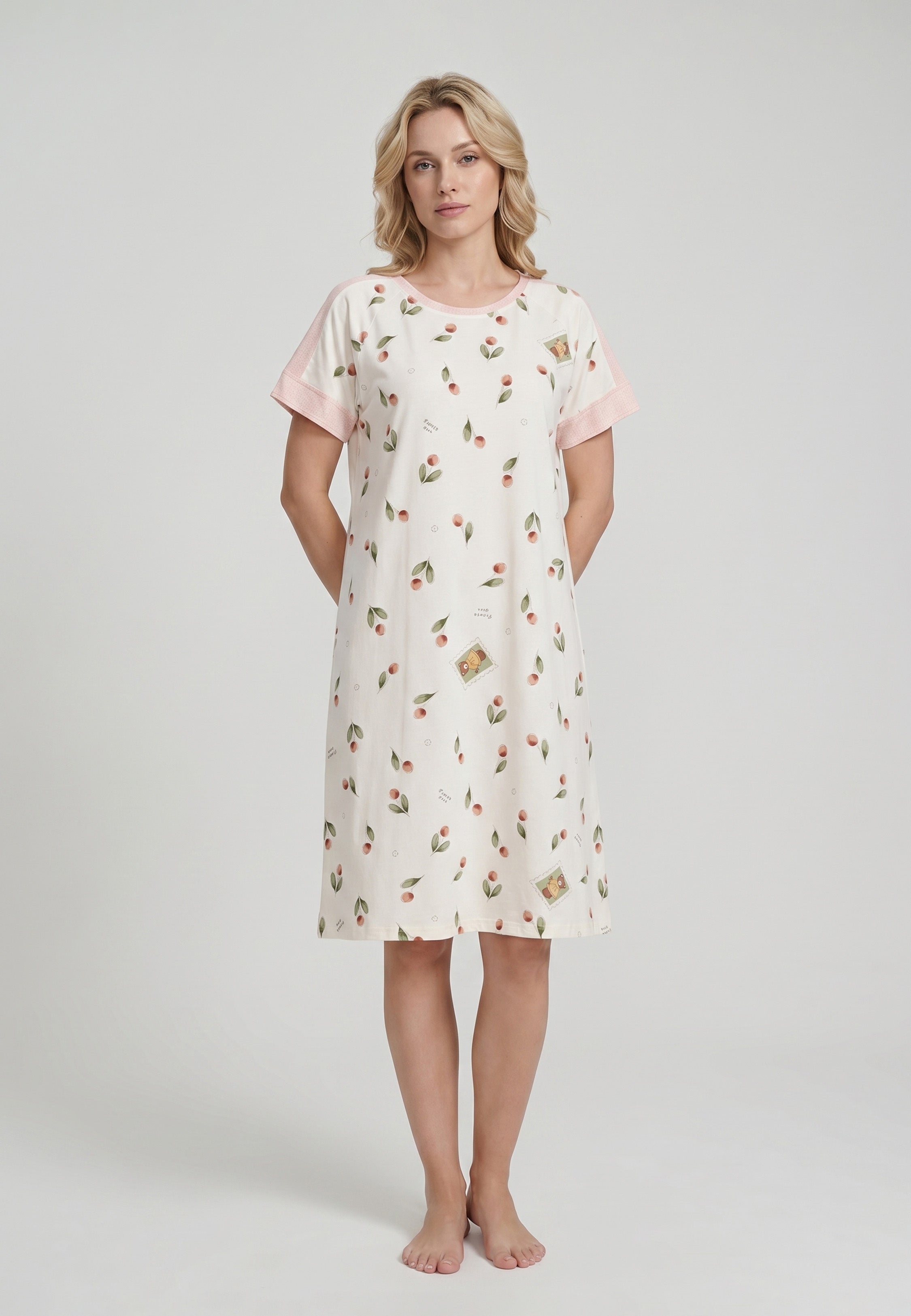 Femme portant une robe de nuit midi col rond manches courtes imprimé cerises et pêches aquarelle fond crème parements contrastants rose poches latérales Rosabella Douceur Cerise