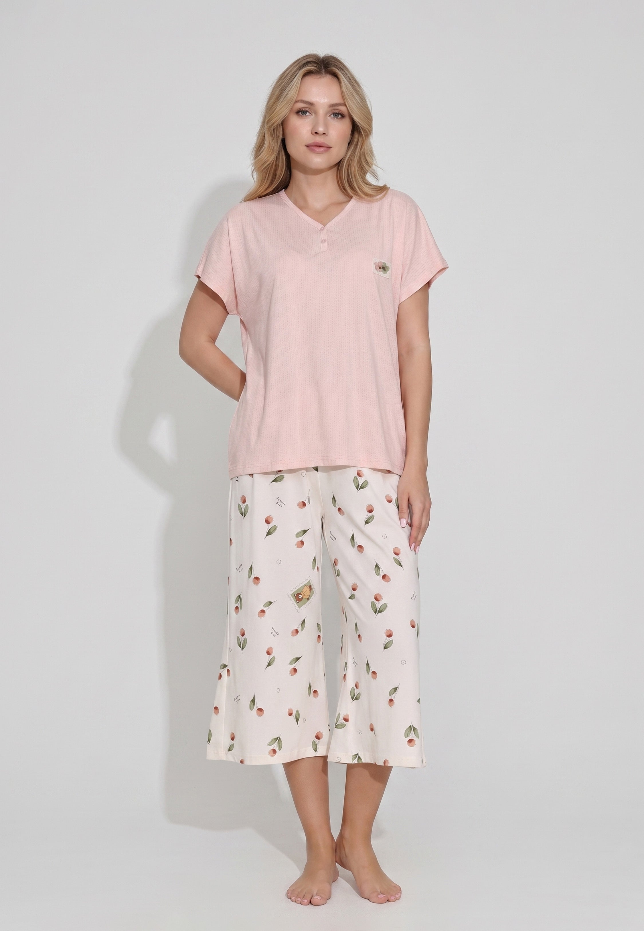 Femme portant un pyjama top col V boutonné manches courtes texturé uni rose badge brodé et pantacourt imprimé cerises et pêches aquarelle fond crème Rosabella Douceur Cerise