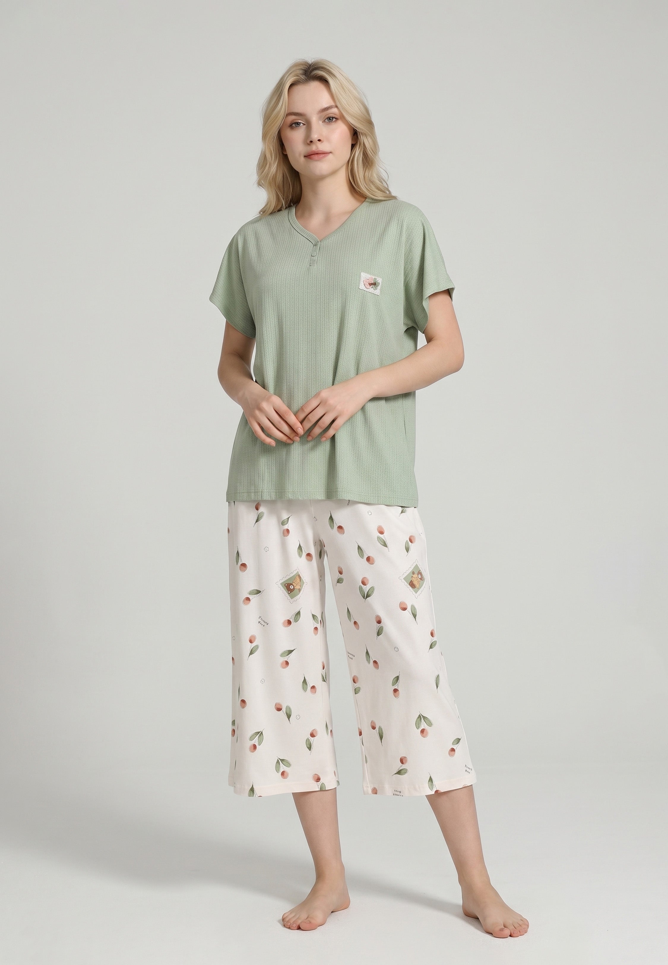 Femme portant un pyjama top col V boutonné manches courtes texturé uni kaki badge brodé et pantacourt imprimé cerises et pêches aquarelle fond crème Rosabella Douceur Cerise