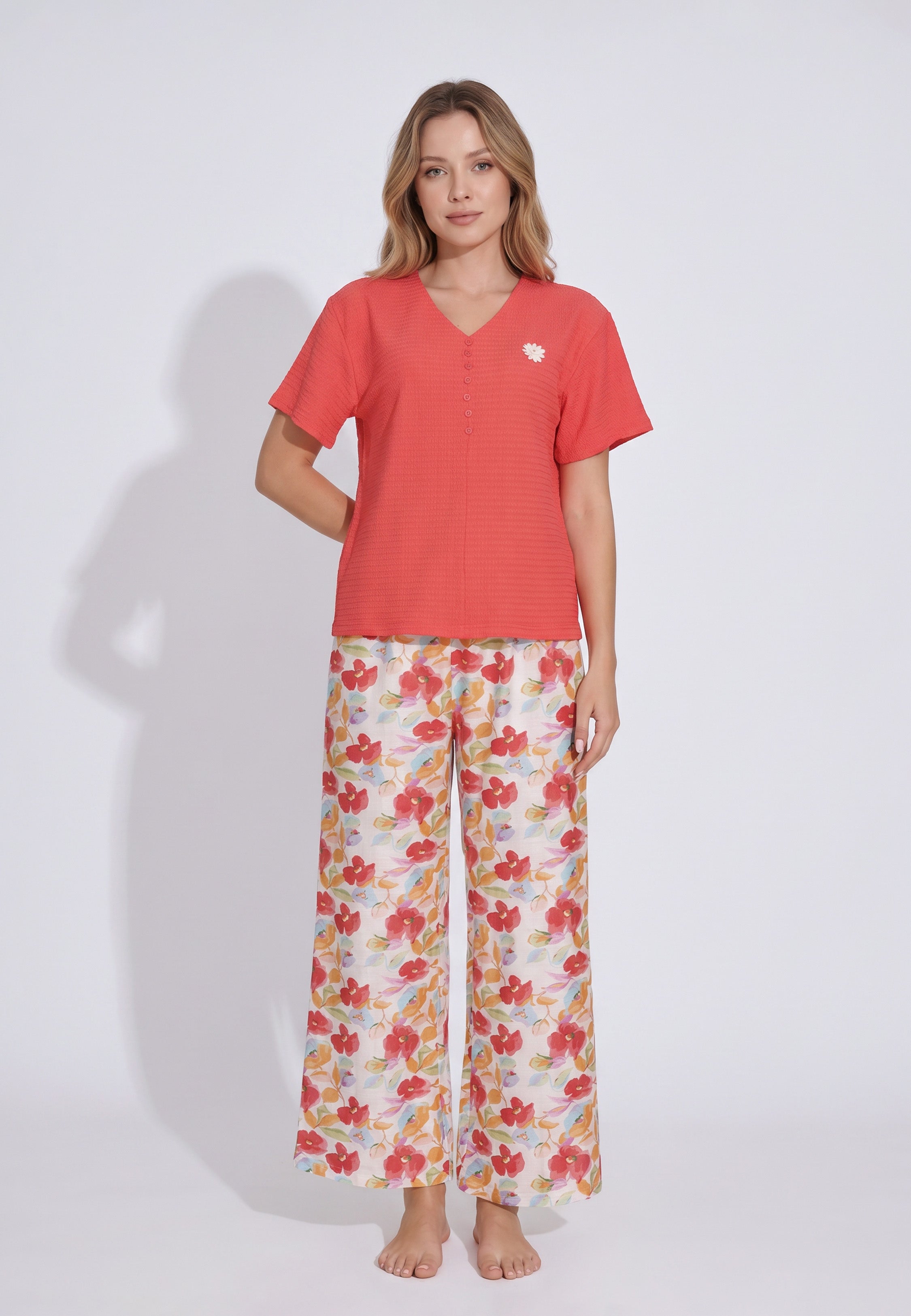 Femme portant un pyjama top col V boutonné manches volantées texturé uni corail badge marguerite brodé et pantalon large grand imprimé fleuri aquarelle multicolore fond blanc Rosabella Rosy Mood