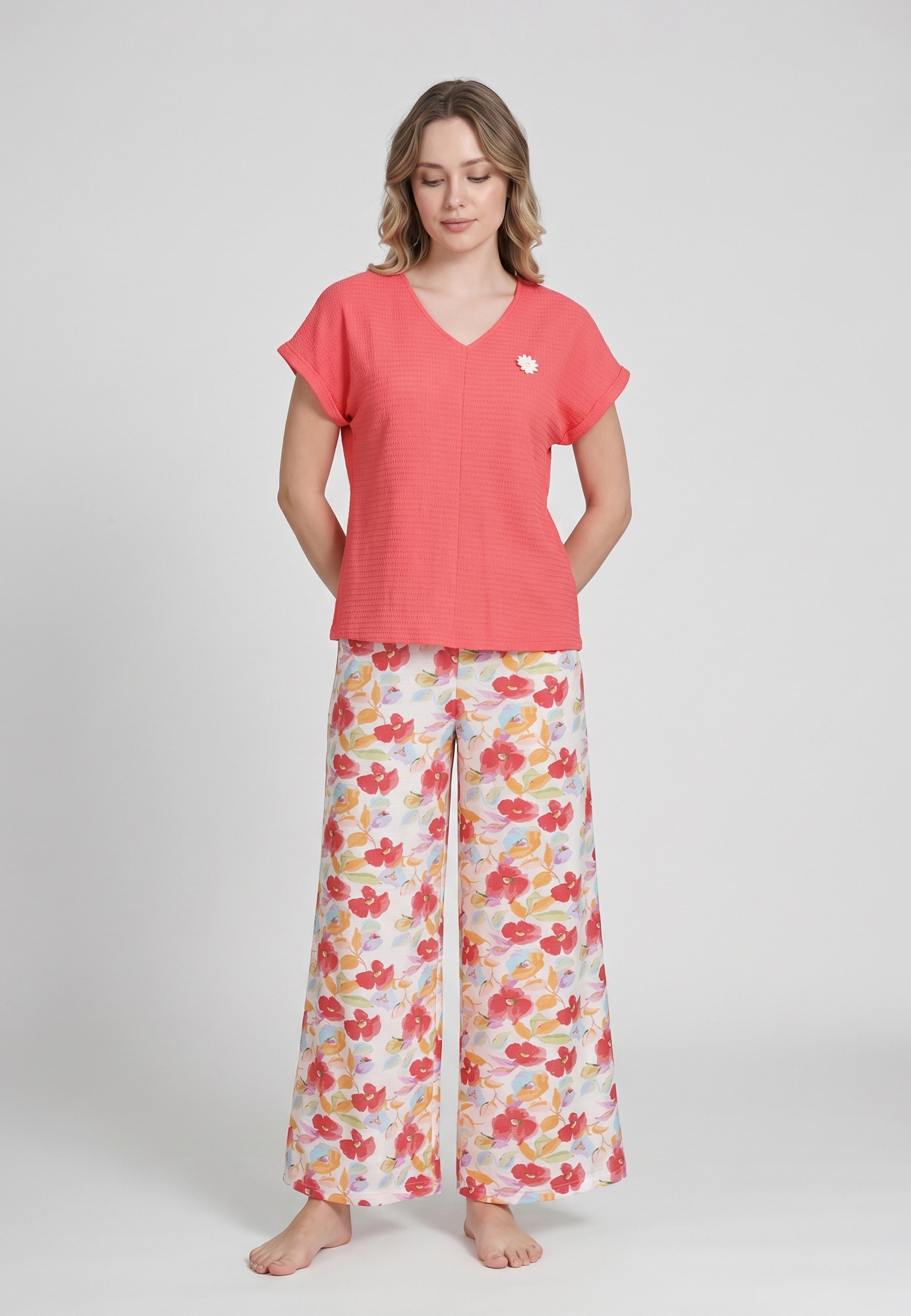 Femme portant un pyjama top col V évasé manches courtes tombantes uni corail badge marguerite brodé et pantalon large grand imprimé fleuri aquarelle multicolore fond blanc Rosabella Rosy Mood