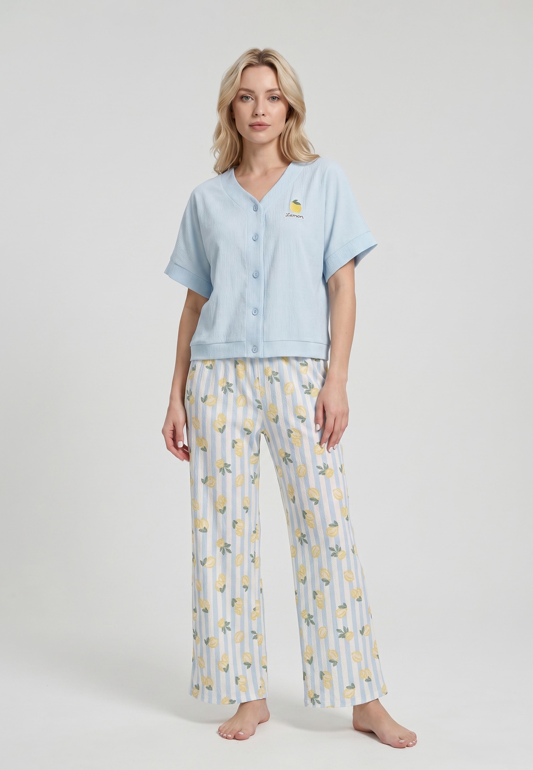 Femme portant un ensemble loungewear top col V boutonné uni bleu ciel badge brodé citron et pantalon large wide-leg rayures bleu ciel blanc imprimé citrons jaunes Rosabella