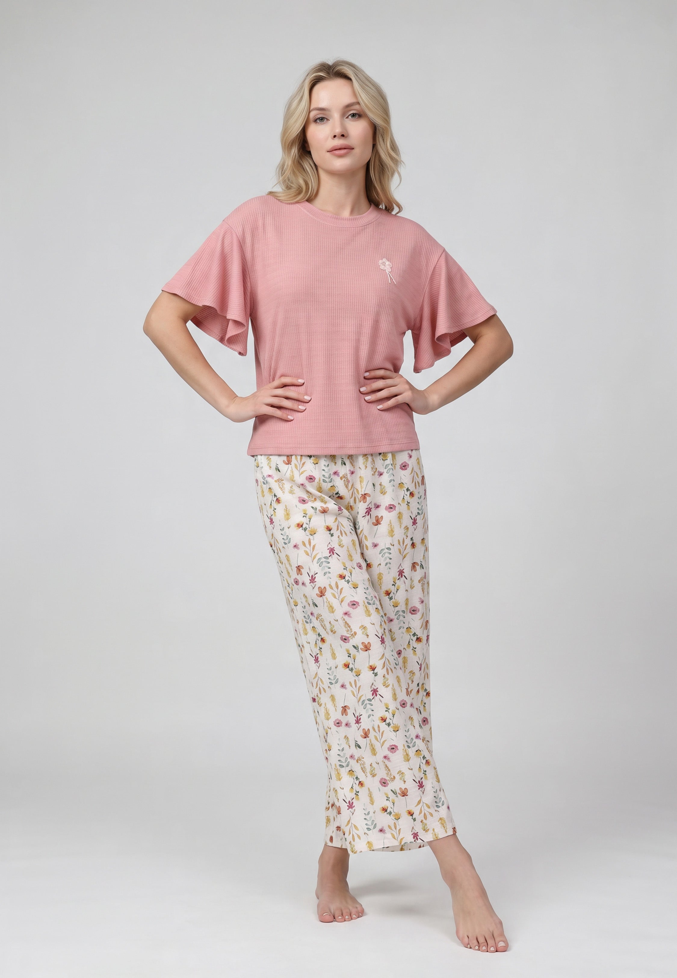 Femme portant un ensemble loungewear top col rond côtelé rose larges volants papillon badge bouquet floral et pantalon large crème imprimé petites fleurs sauvages multicolores Rosabella
