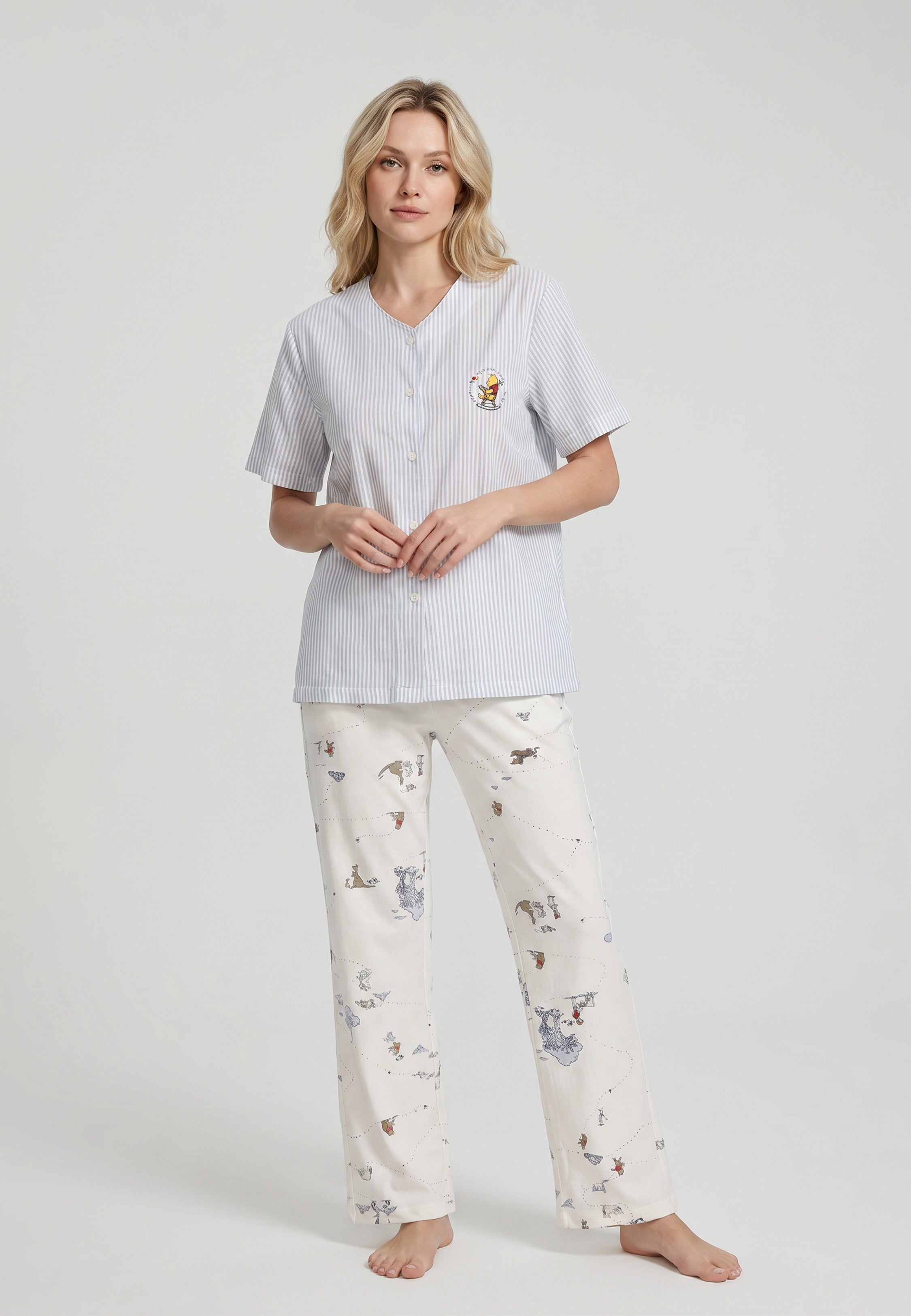 Femme portant un ensemble pyjama top col V boutonné seersucker rayé bleu ciel poche patchée et pantalon imprimé all-over fond crème Rosabella