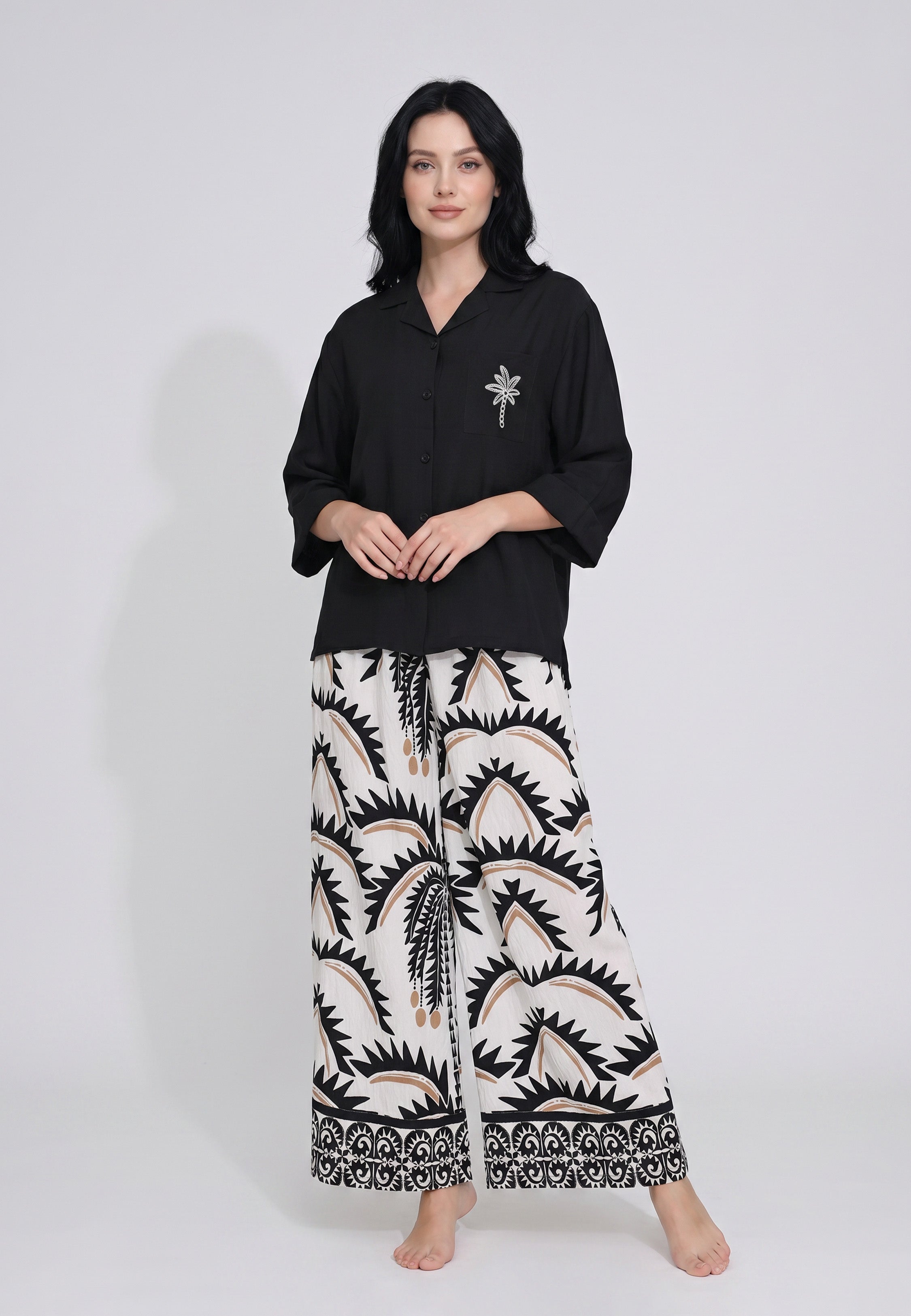Femme portant un ensemble chemise camp noire manches 3/4 badge palmier strass argenté et pantalon large imprimé palmiers tribaux ivoire crème camel Rosabella