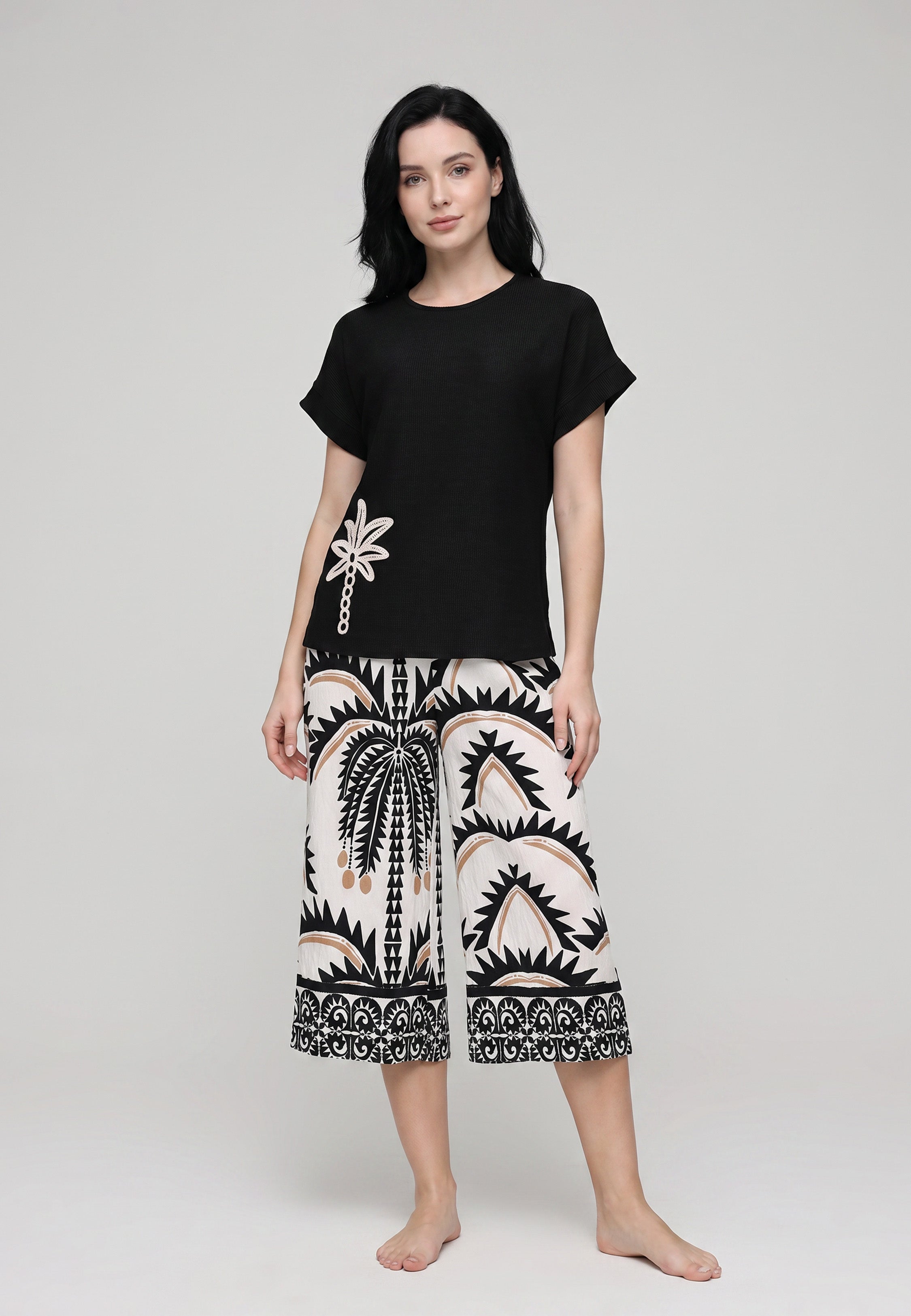 Femme portant un ensemble top col rond crop noir badge palmier brodé et pantacourt large imprimé palmiers tribaux ivoire crème camel Rosabella