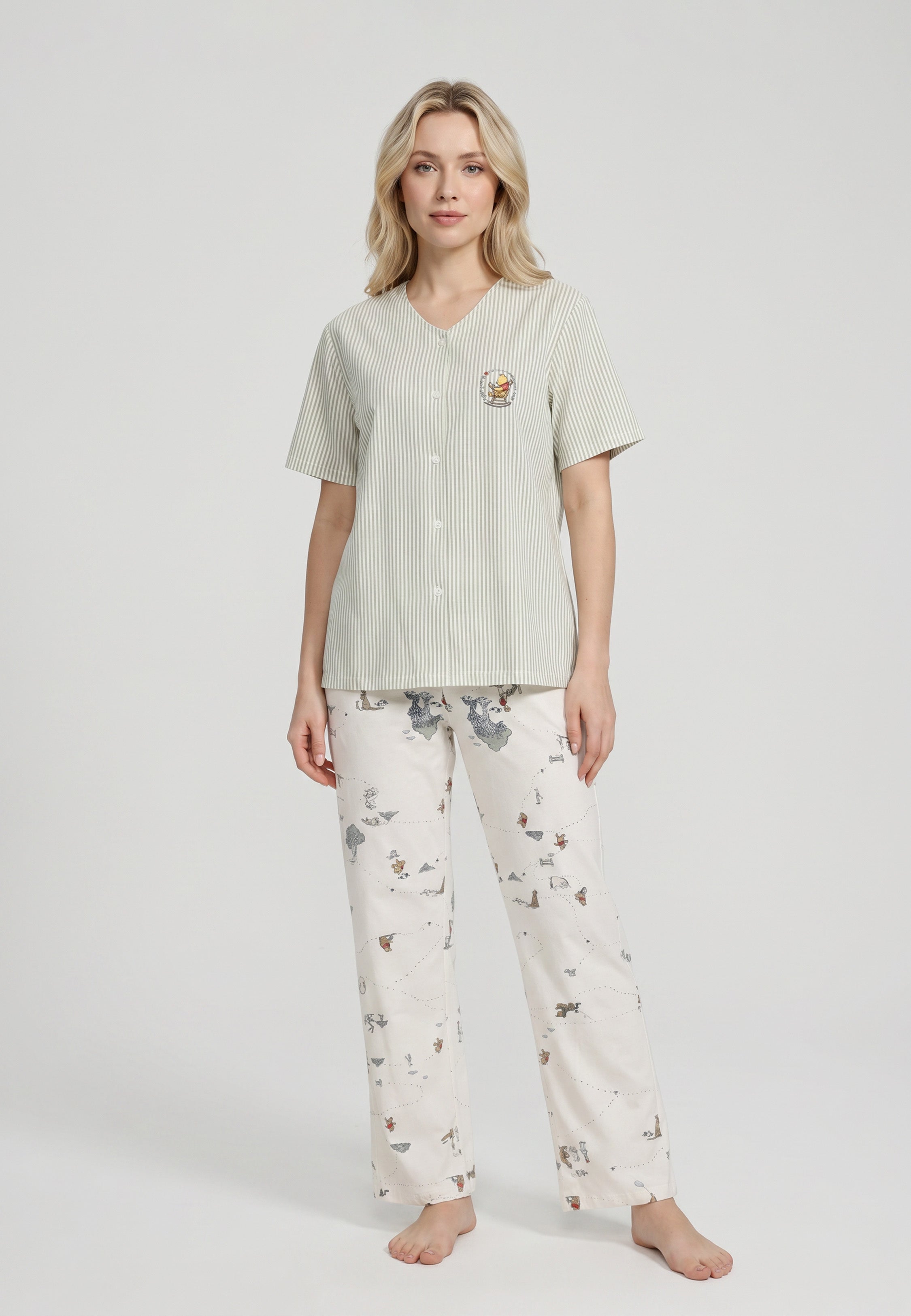 Femme portant un ensemble pyjama top col V boutonné seersucker rayé vert sauge poche patchée et pantalon imprimé all-over fond crème Rosabella